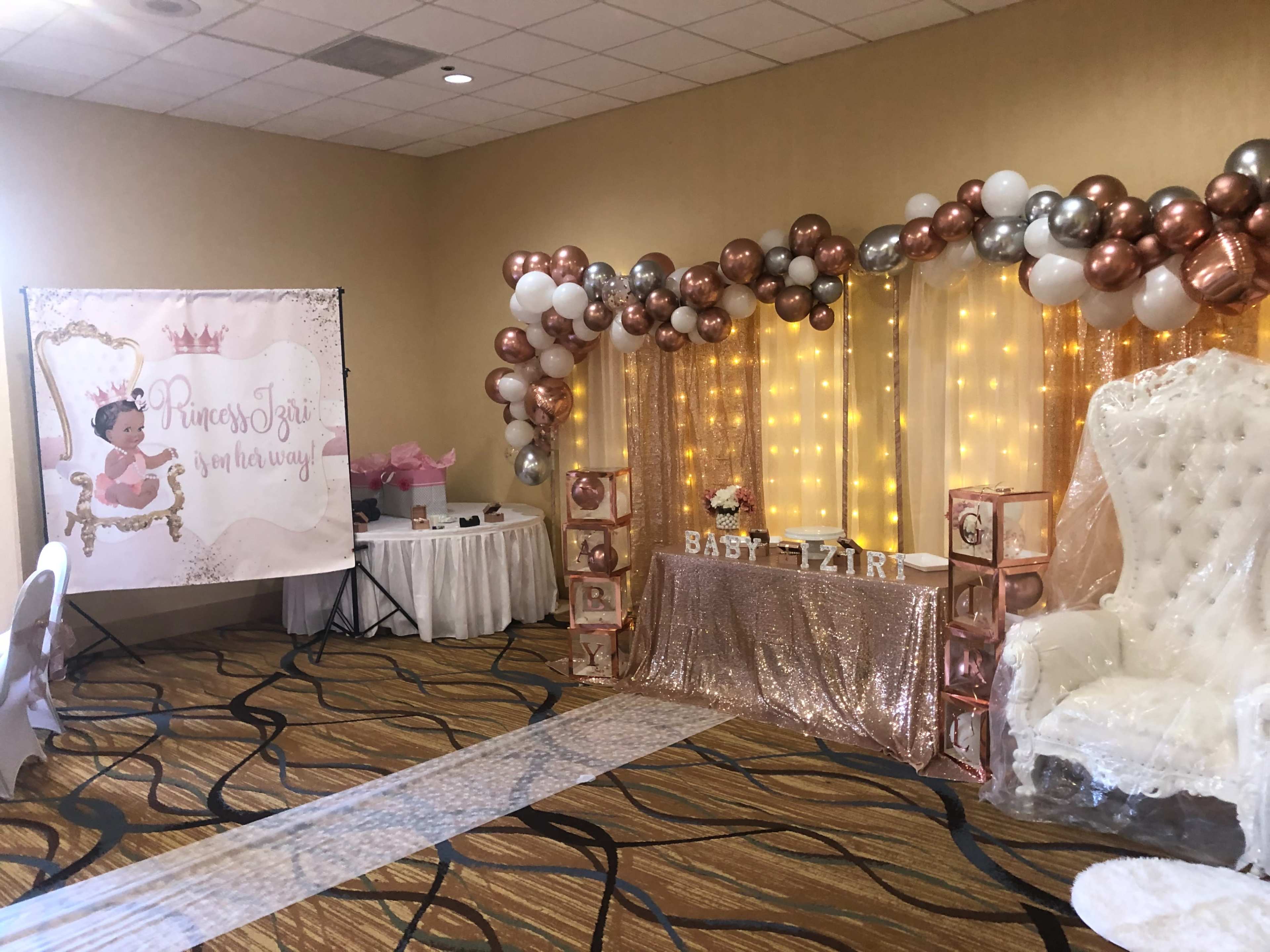 A decorated event space features a "Princess" themed backdrop, a table with golden letters spelling "BABY ZIR" and a plush white throne, surrounded by balloons and fairy lights.