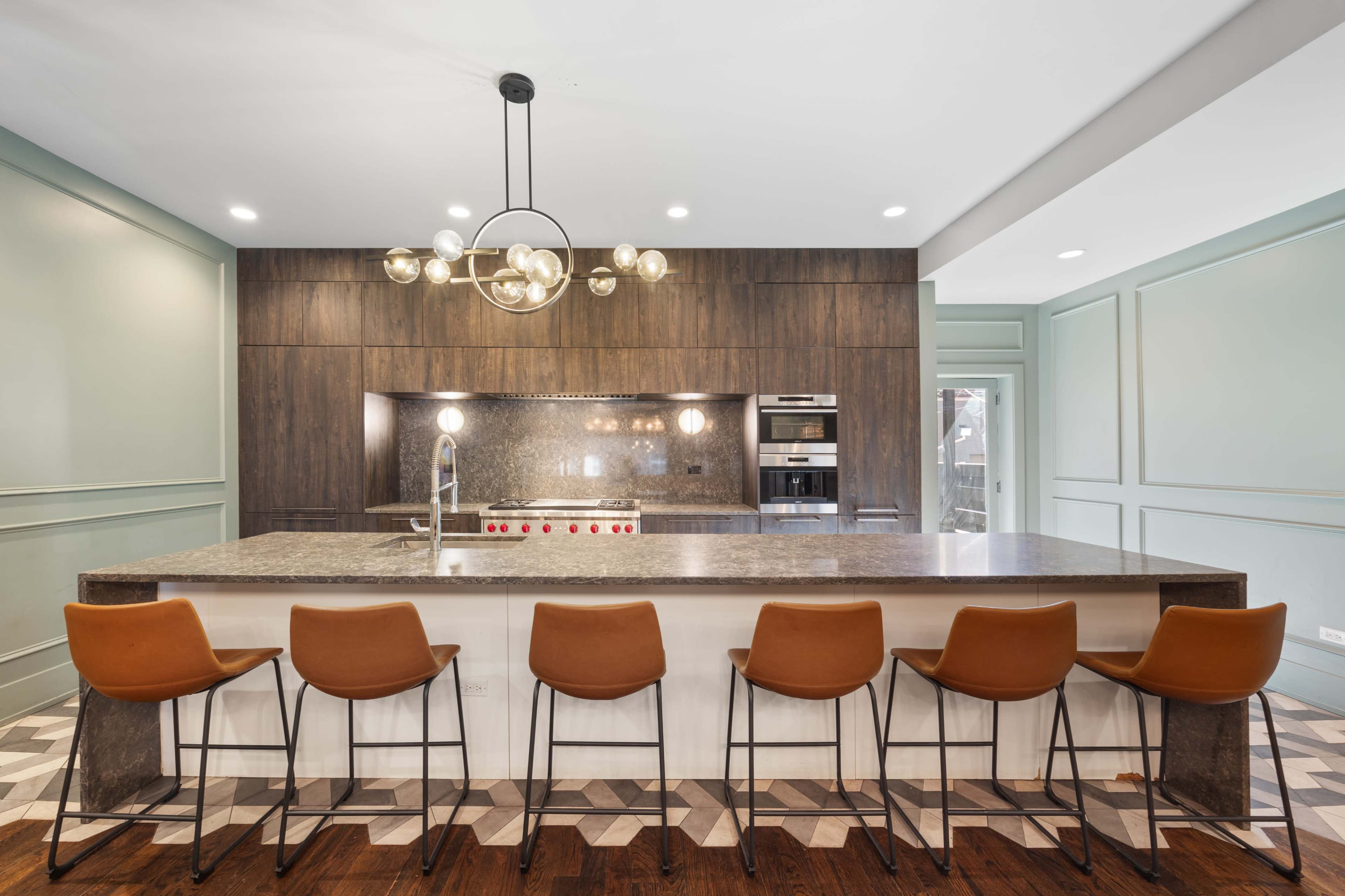 A modern kitchen features a large island with seating, elegant cabinetry, and stainless steel appliances.