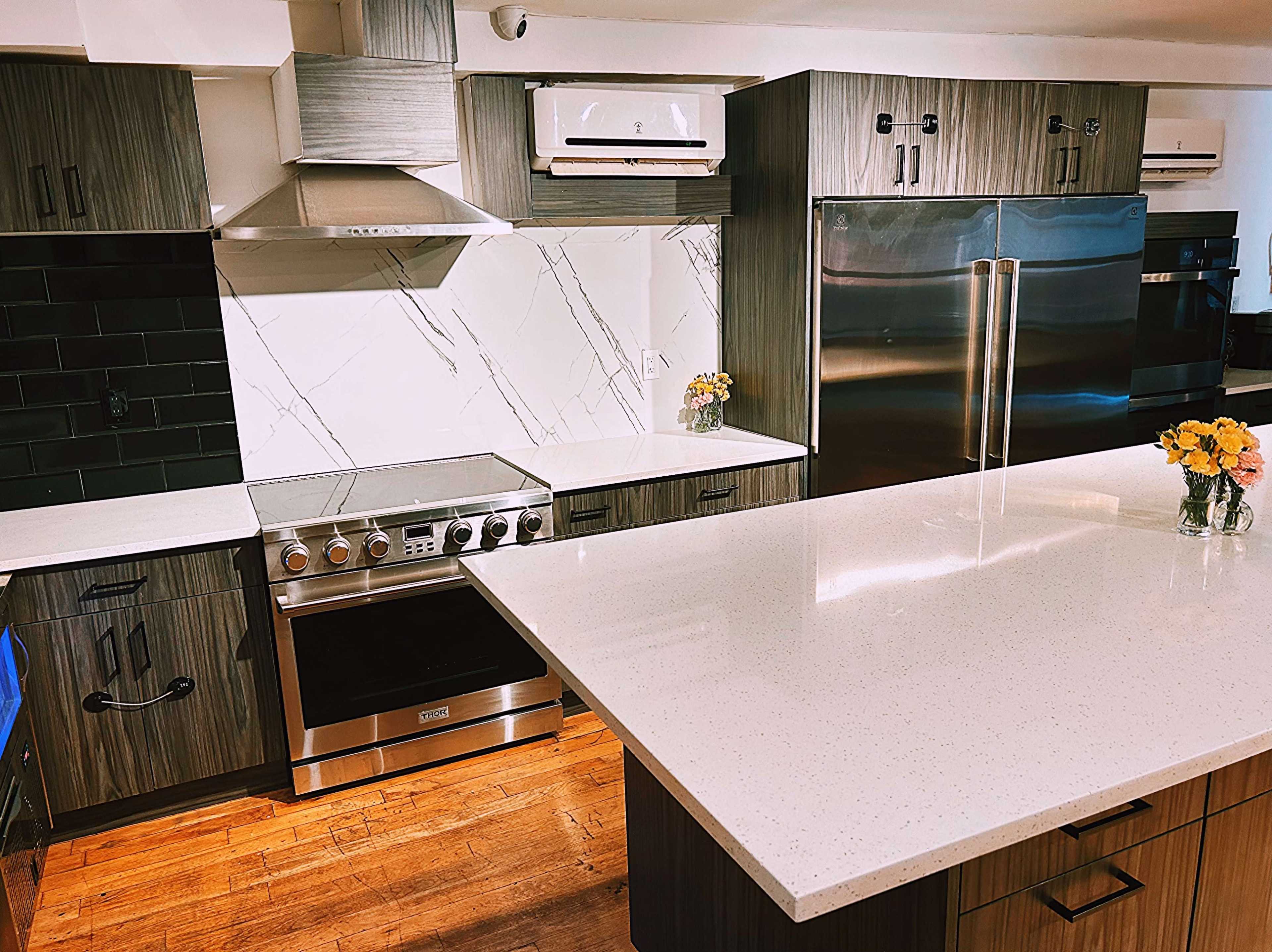 The image shows a modern kitchen with dark wood cabinetry, stainless steel appliances, a large island with a quartz countertop, and a floral centerpiece.