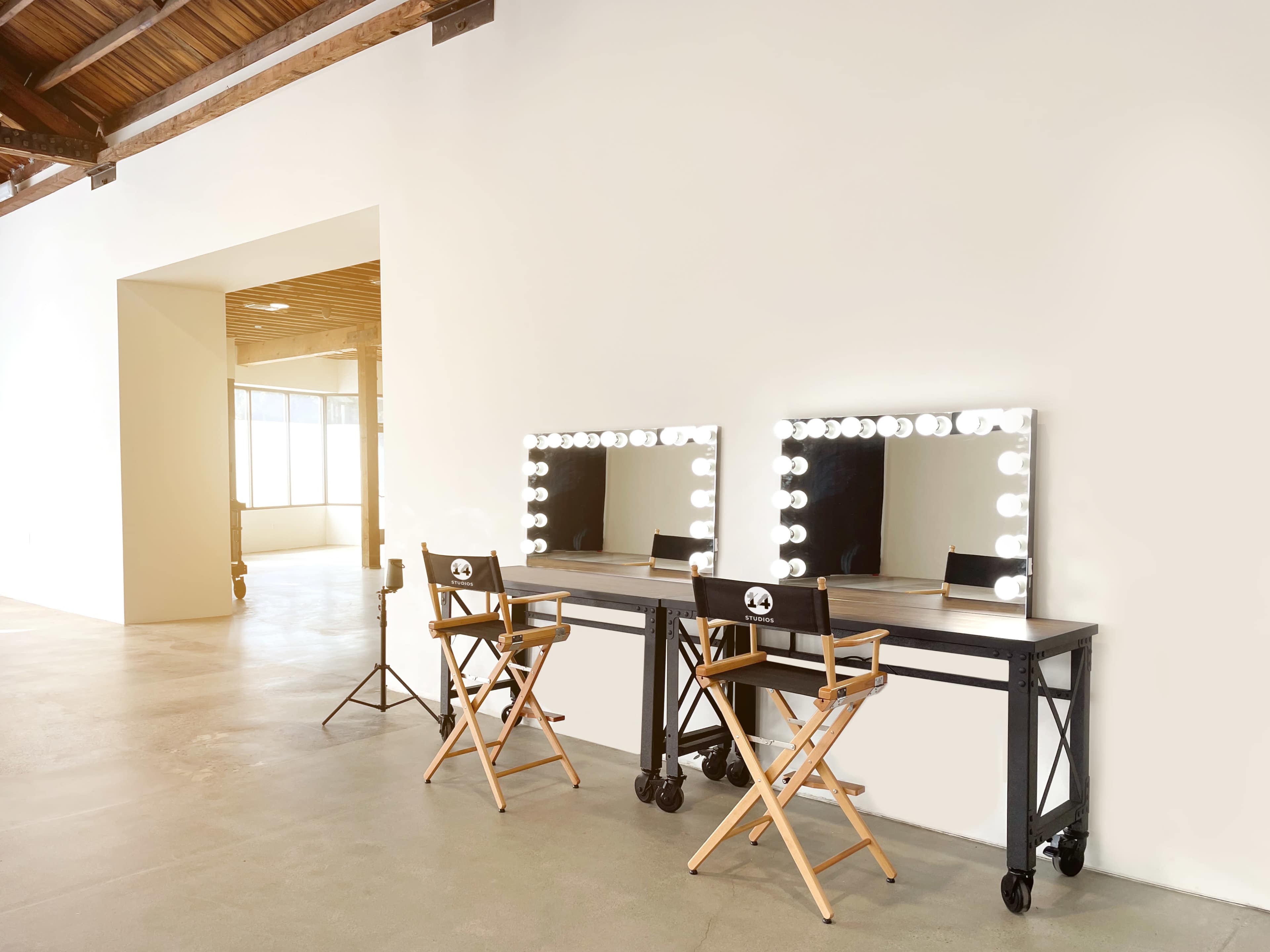 Two makeup stations with illuminated mirrors and director's chairs in a spacious, lightly furnished room.