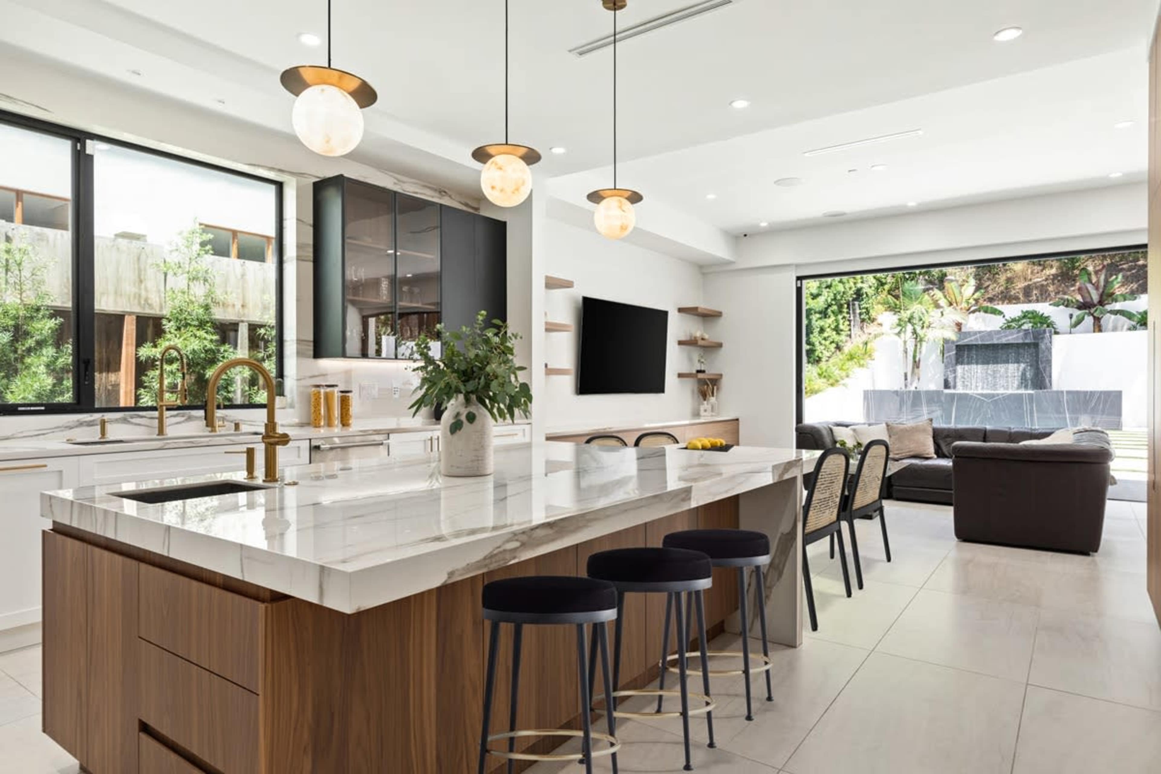 A modern kitchen with a large island, contemporary bar stools, and a glass door leading to an outdoor seating area.