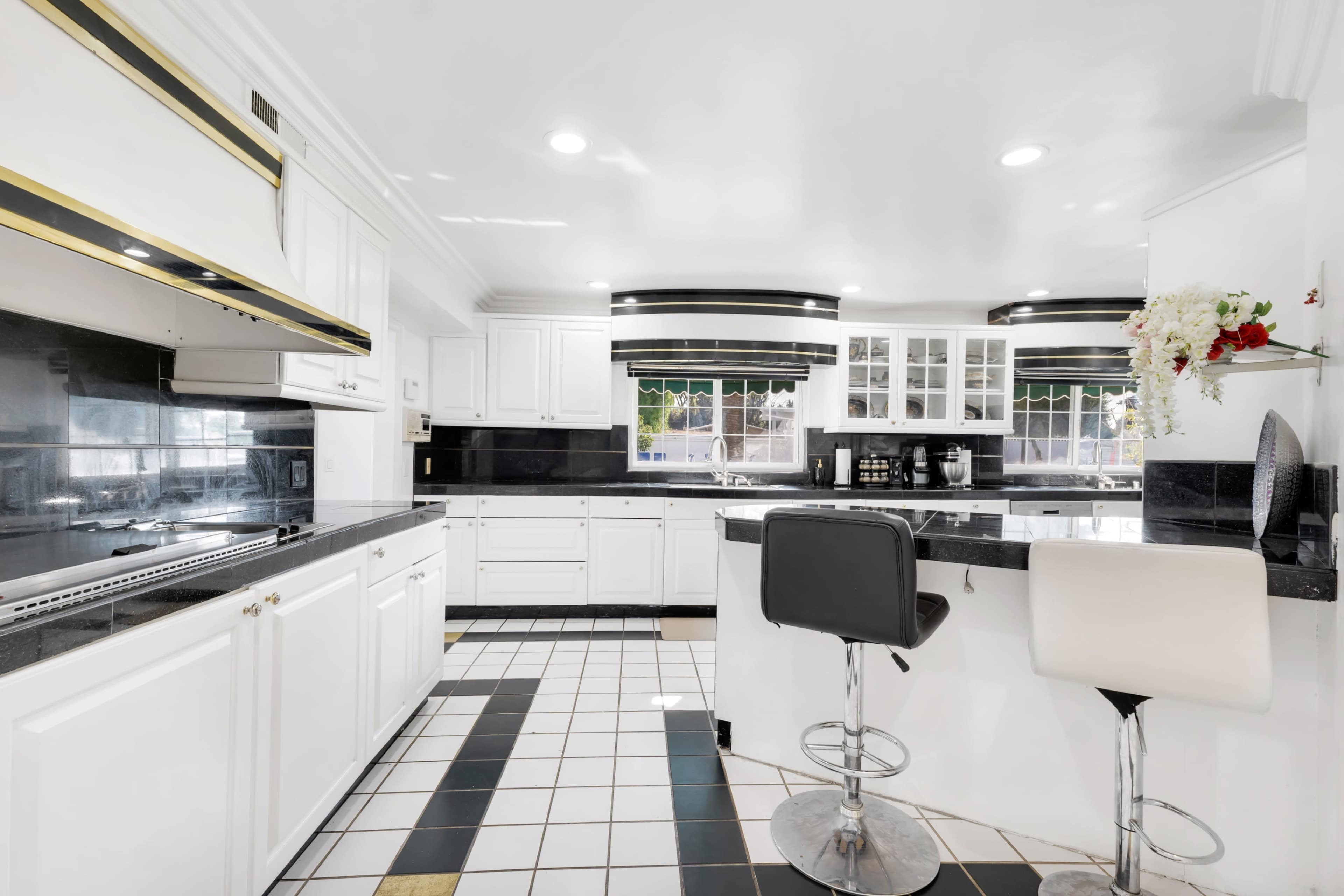 The image shows a modern kitchen with white cabinets, black countertops, and a tiled floor featuring a geometric pattern.