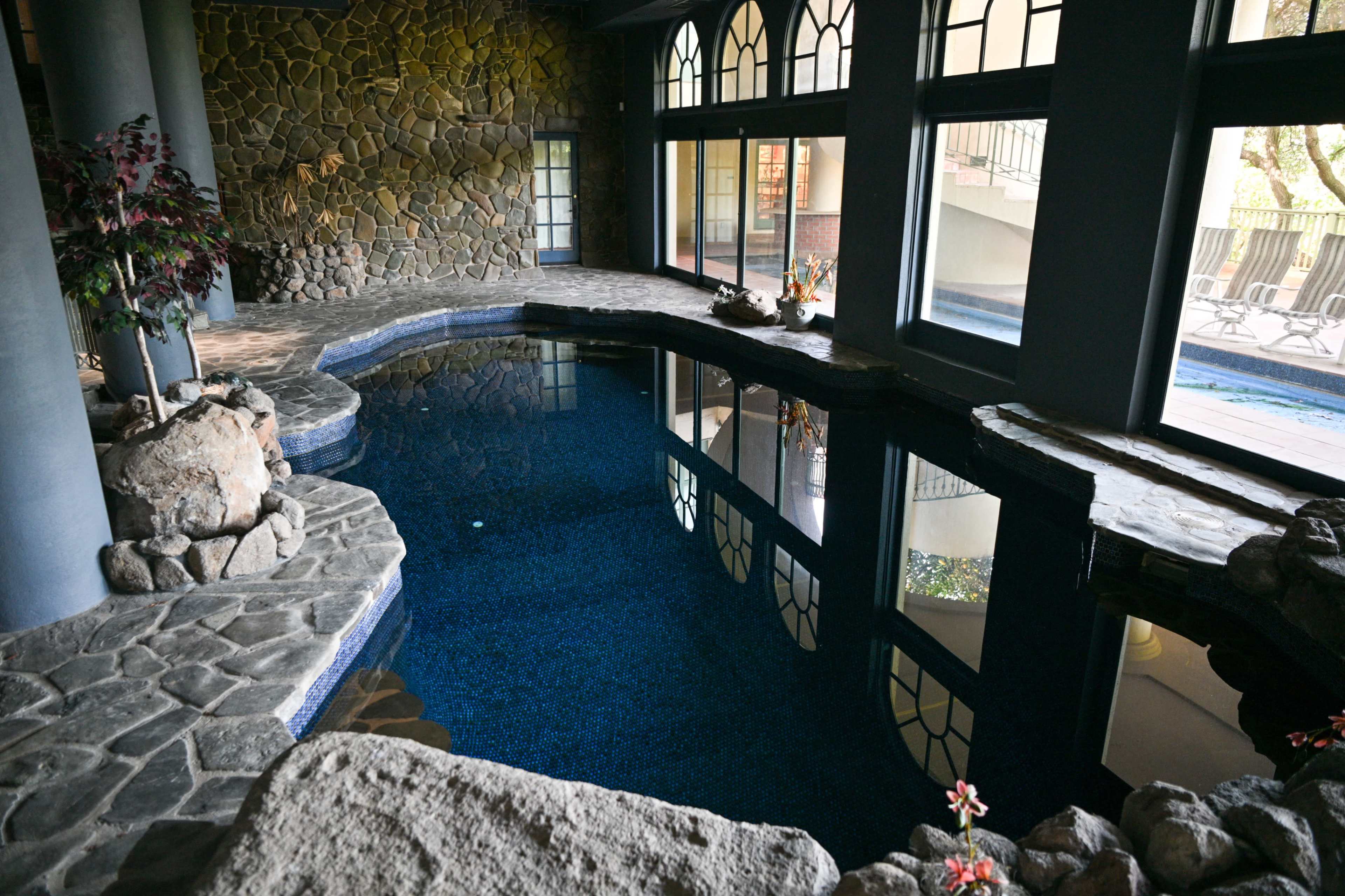 The image shows a stone-enclosed indoor pool area with large windows and a smooth, tiled floor.