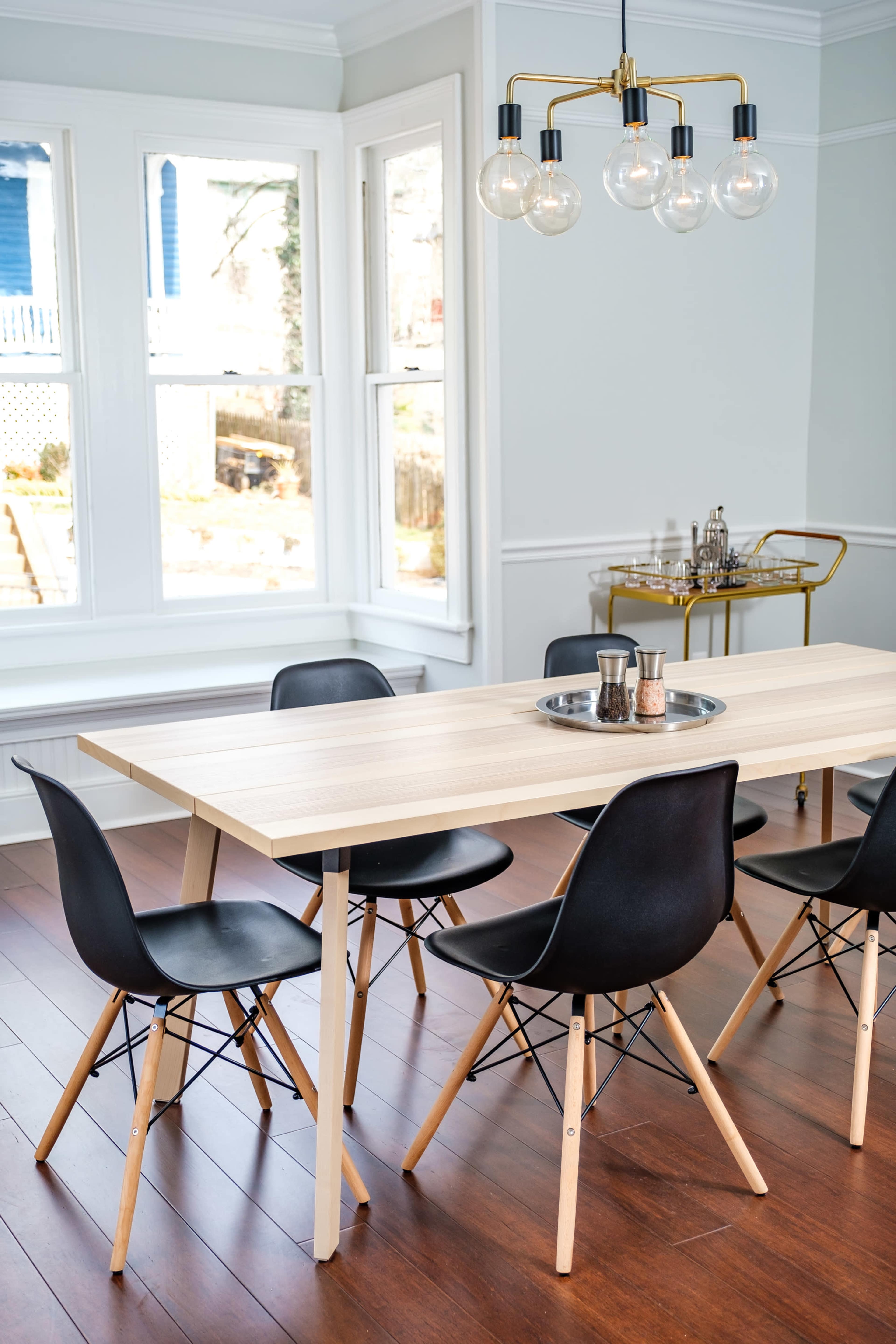 A modern dining area features a rectangular wooden table surrounded by black chairs, illuminated by a hanging light fixture.