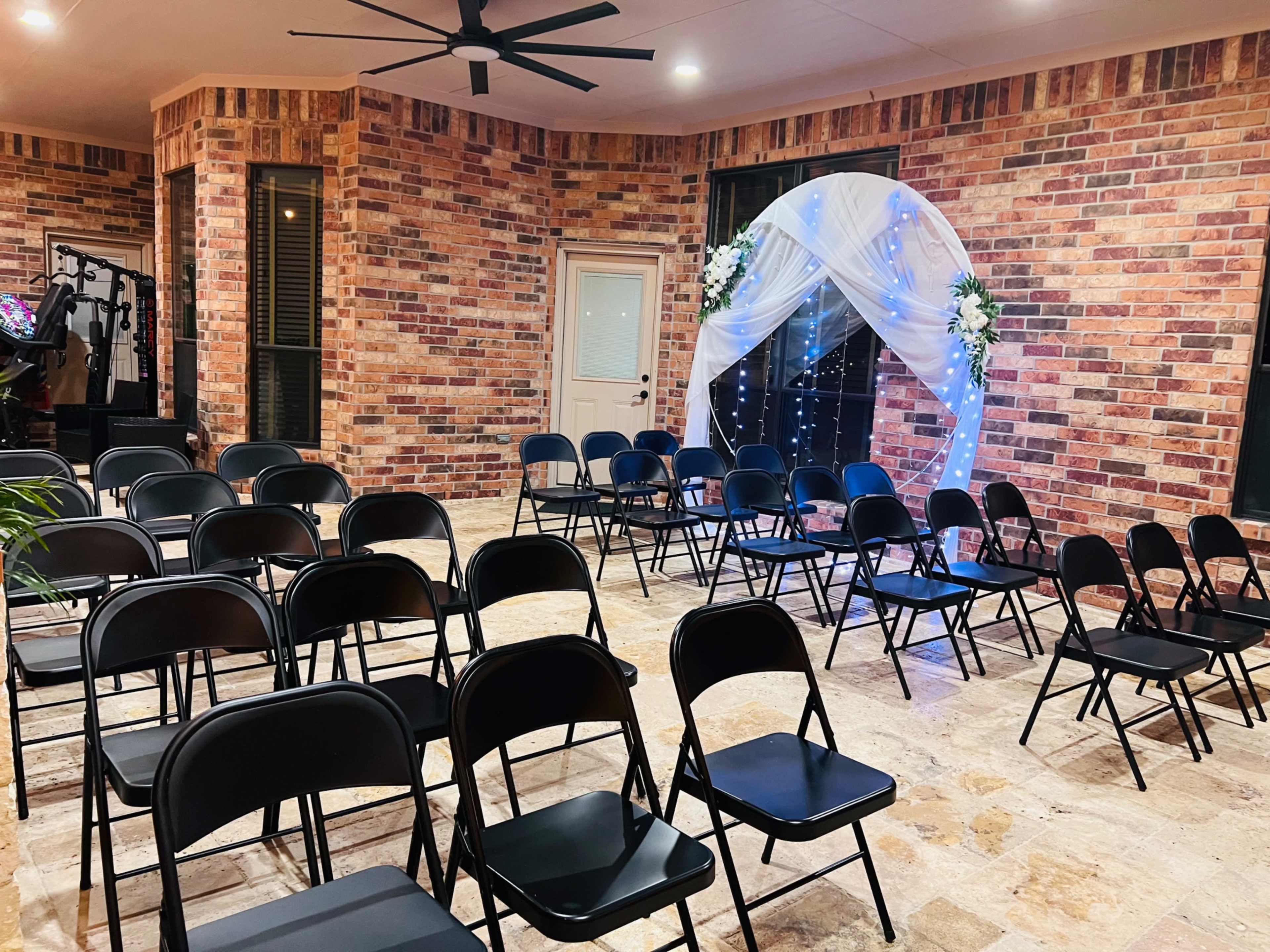 The image shows a room with black folding chairs arranged in rows facing a decorated archway draped in white fabric and illuminated by blue lights.