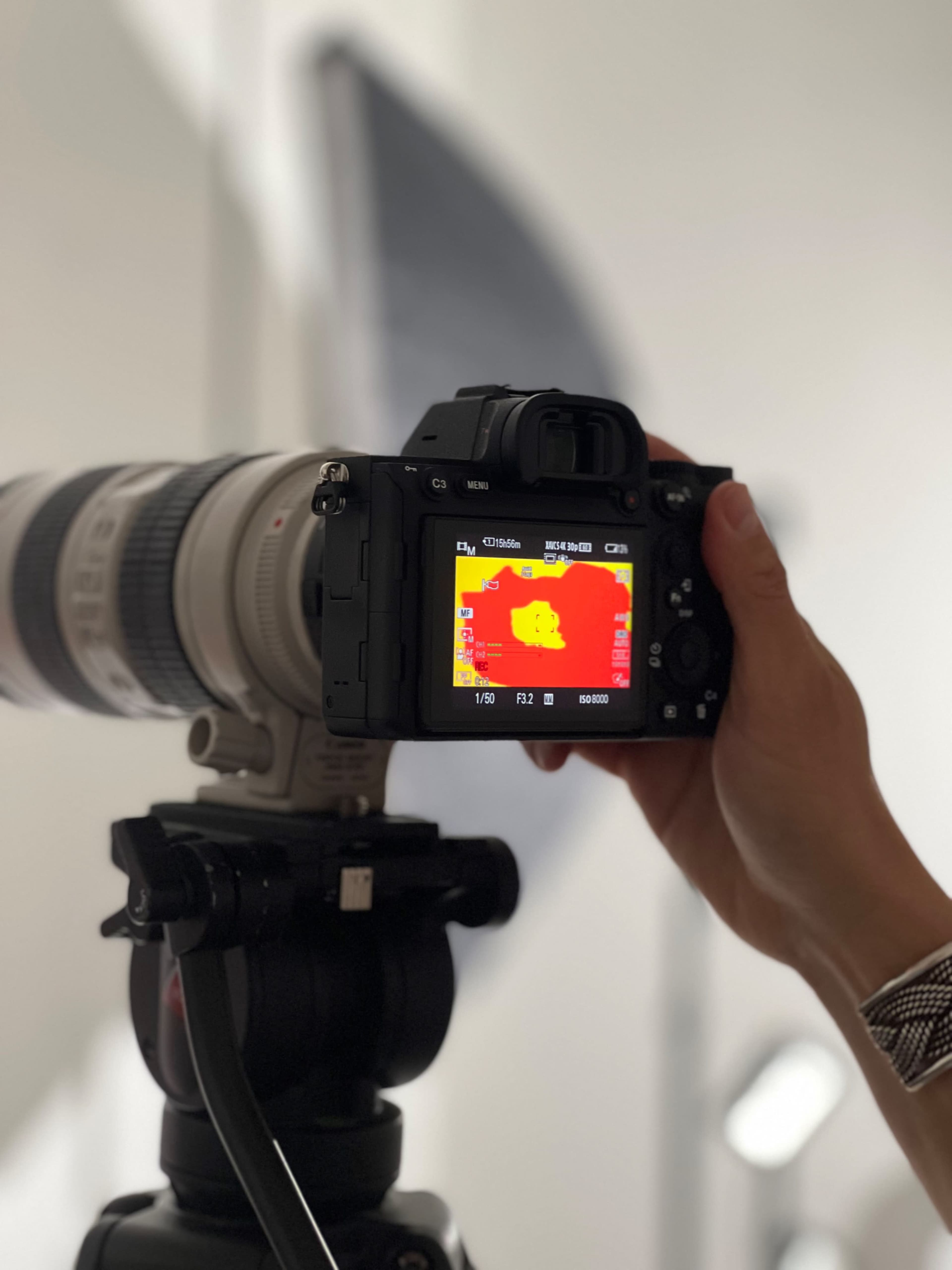 A person holds a camera with a telephoto lens, displaying a thermal image on its screen.