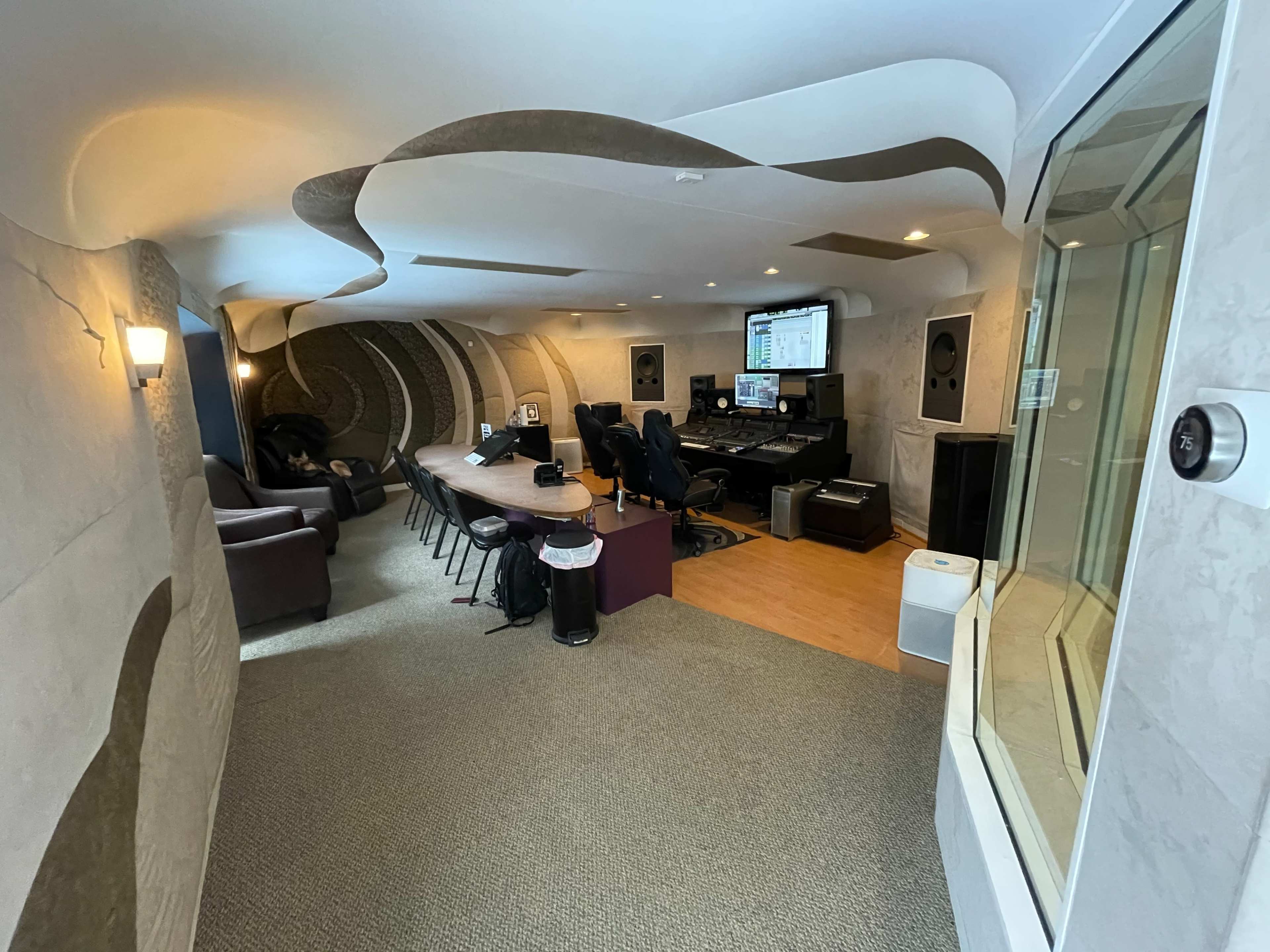 A modern recording studio featuring an elongated room with a sound mixing area, seating, and glass-walled isolation space.