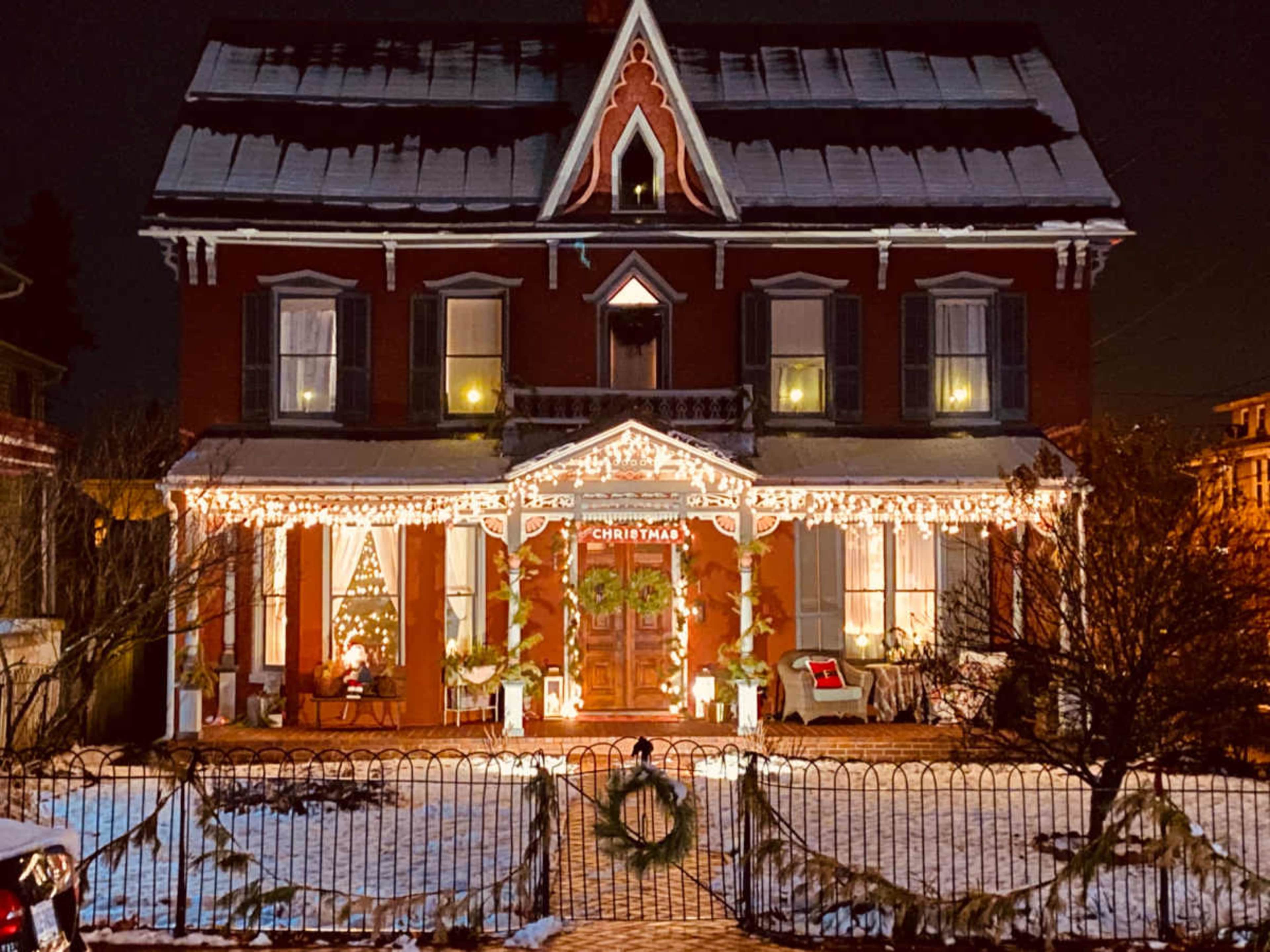 A decorated Victorian house with Christmas lights and a snow-covered yard.