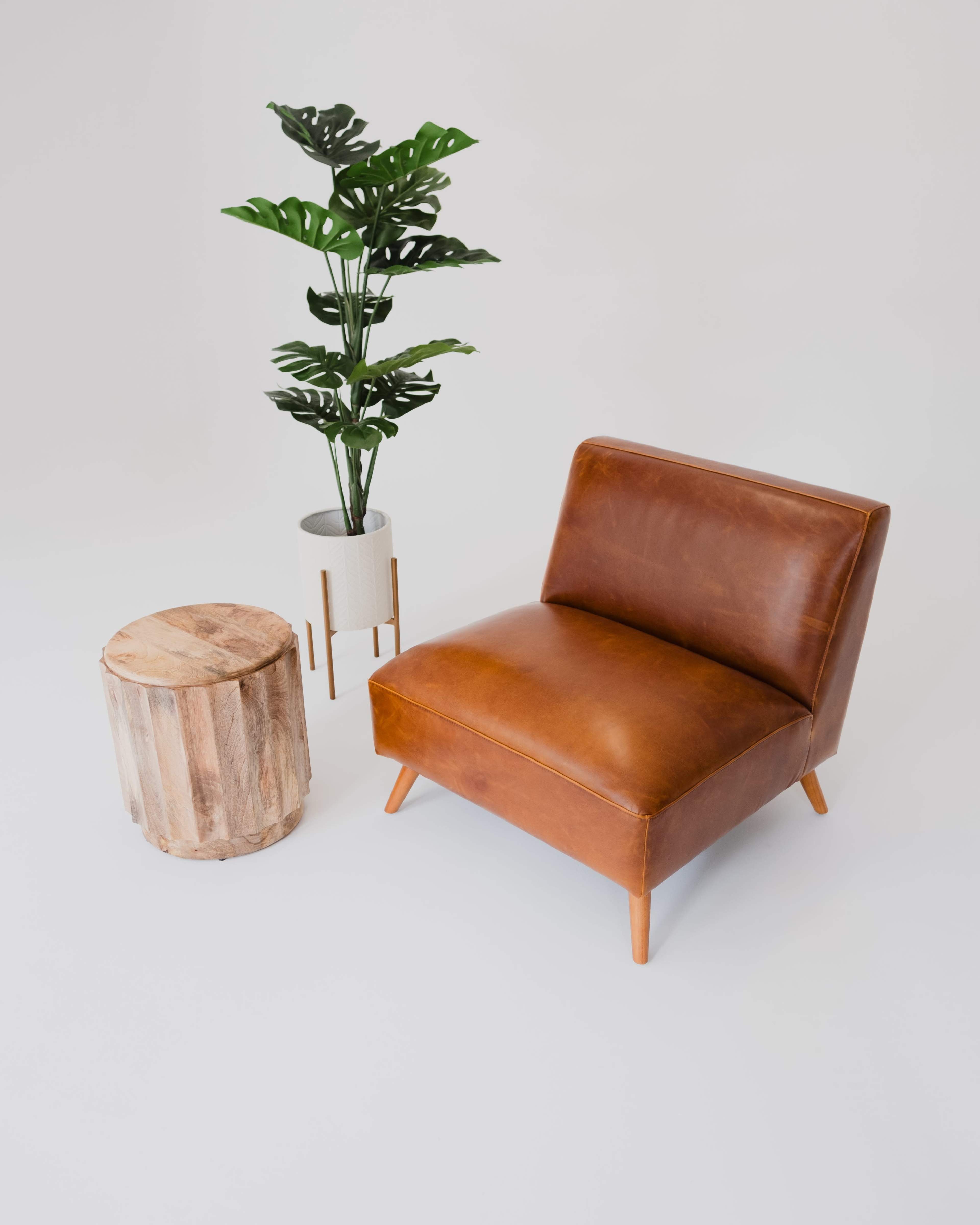 A brown leather chair beside a wooden stool and a potted plant.