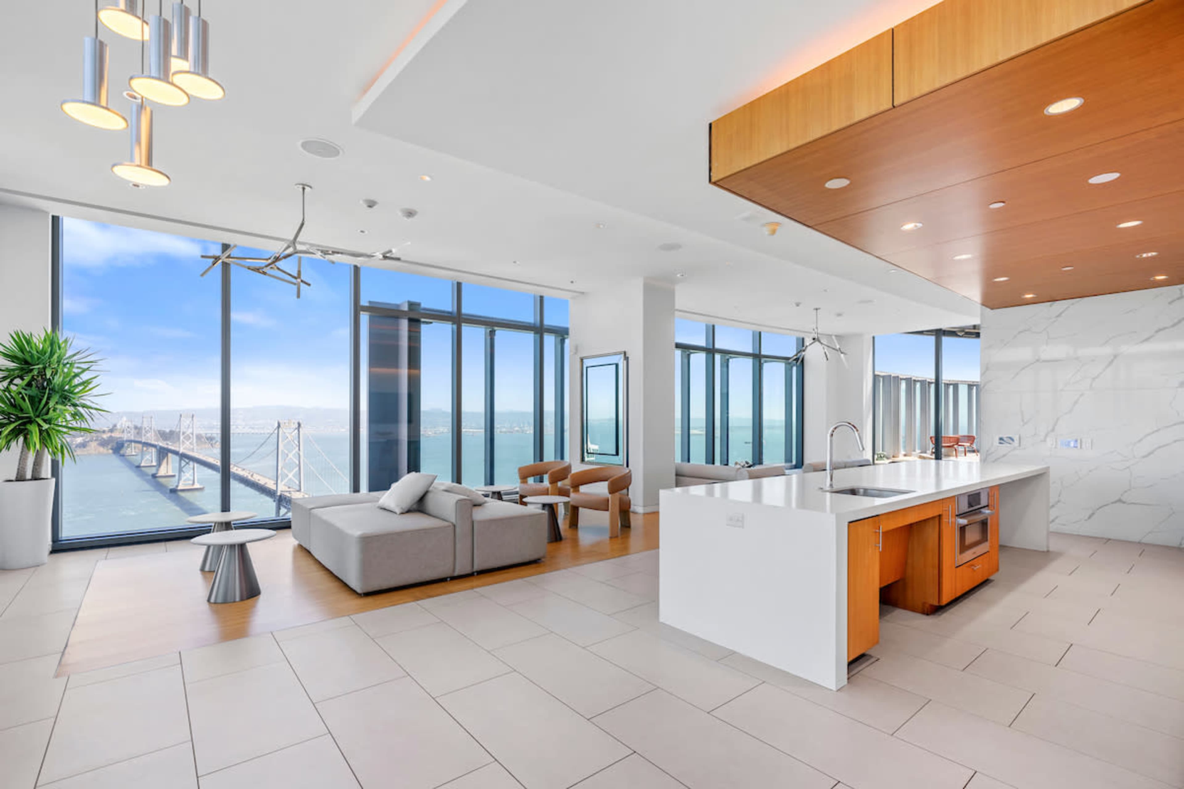 A modern, open-concept living space features a sleek kitchen and a seating area with large windows offering views of a bridge and water.