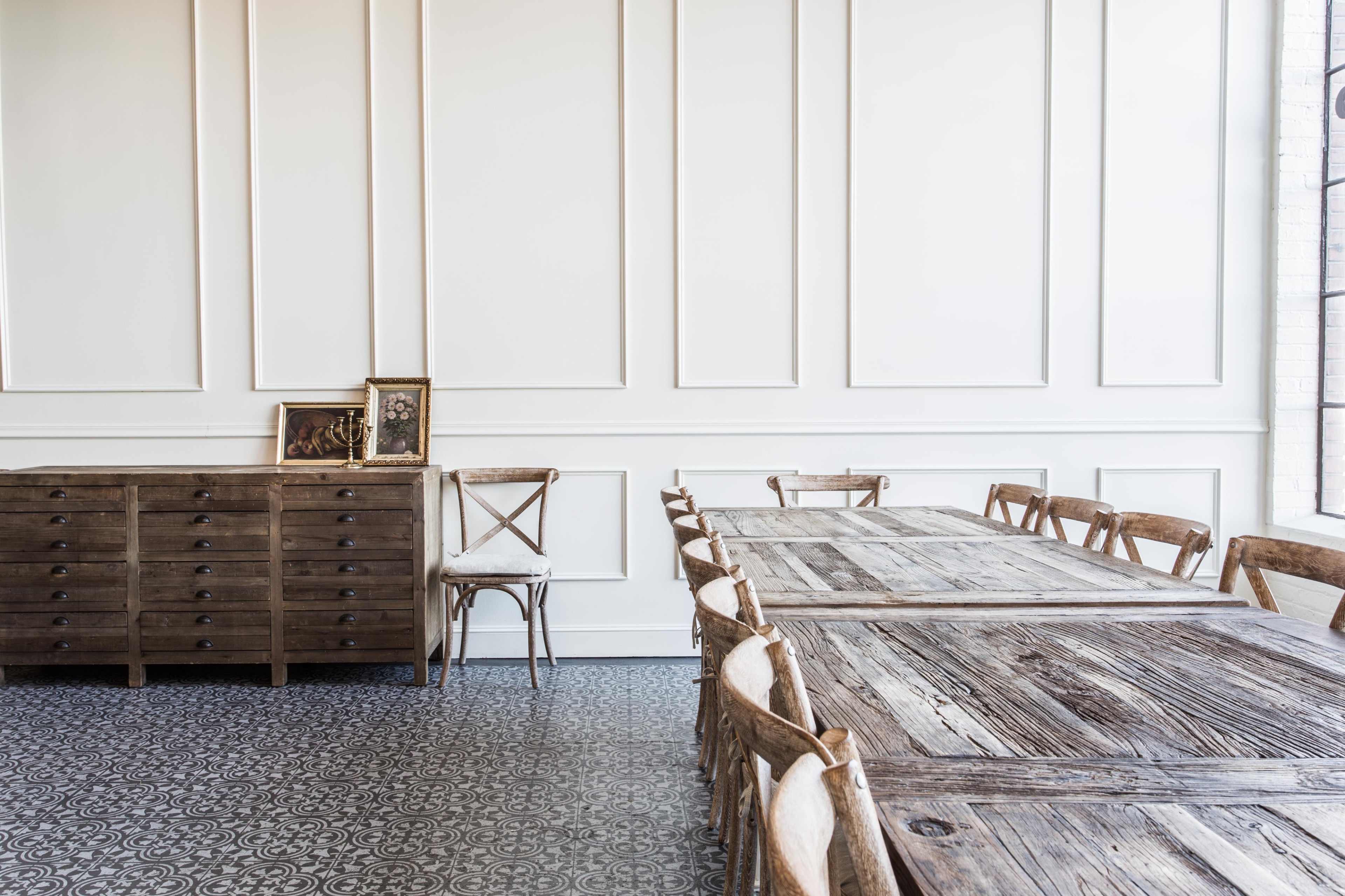 A spacious room with wooden furniture, featuring a long dining table and a matching sideboard against a wall with decorative paneling.