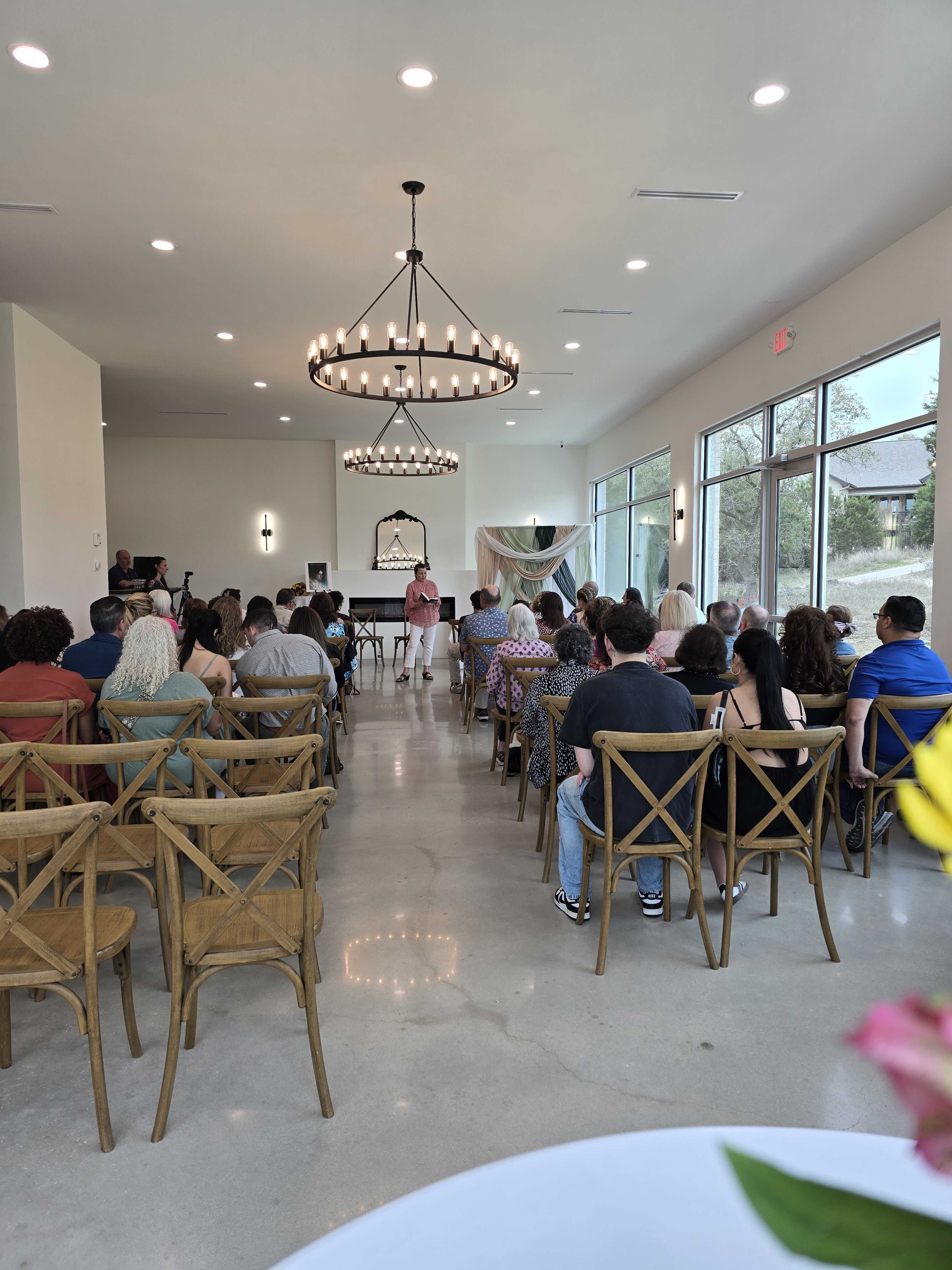 A crowd of people is seated in a modern event space, facing a speaker at the front near a decorative backdrop.