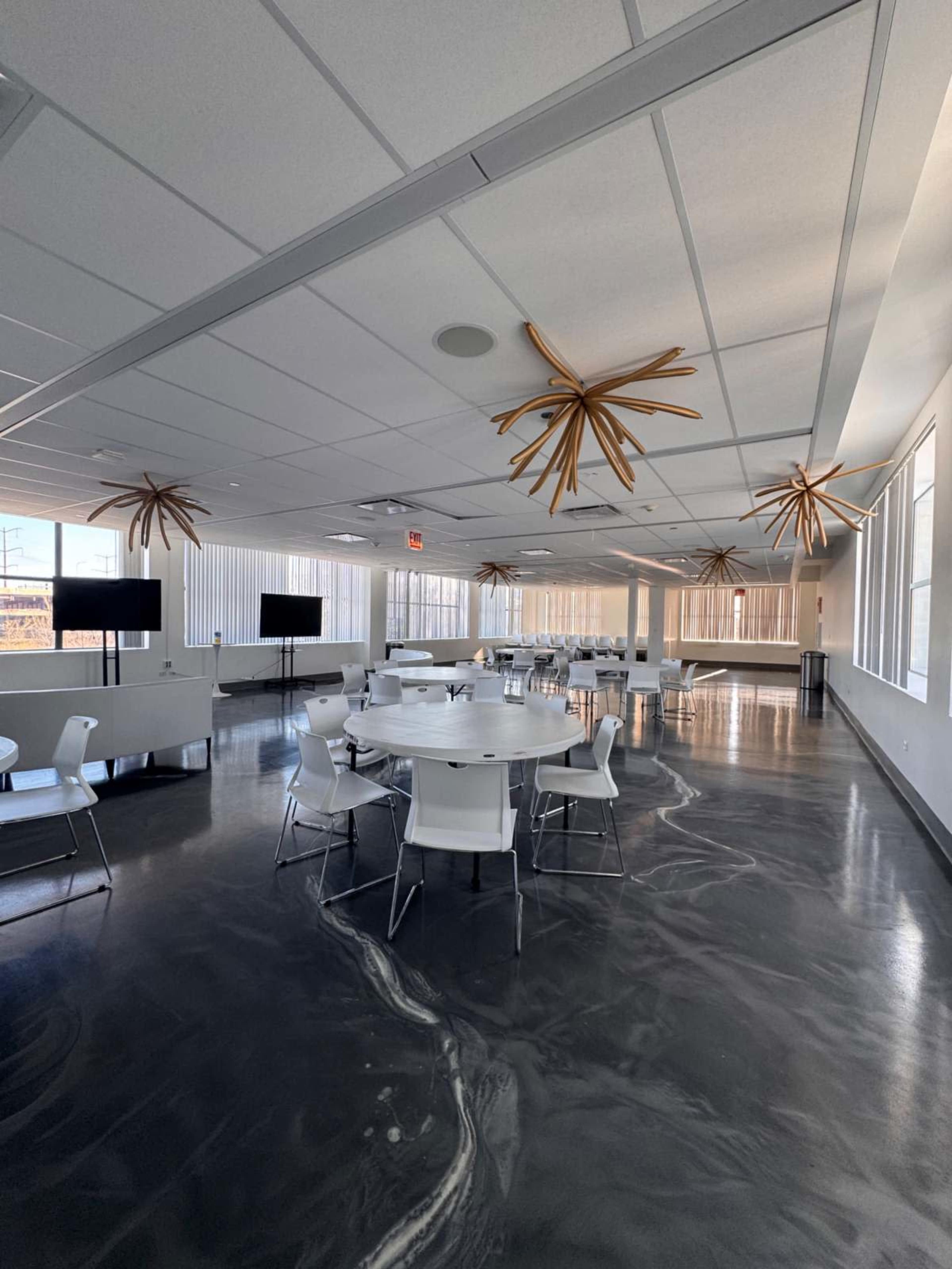 The image shows a modern meeting room with several round tables and chairs, illuminated by unique ceiling fixtures.