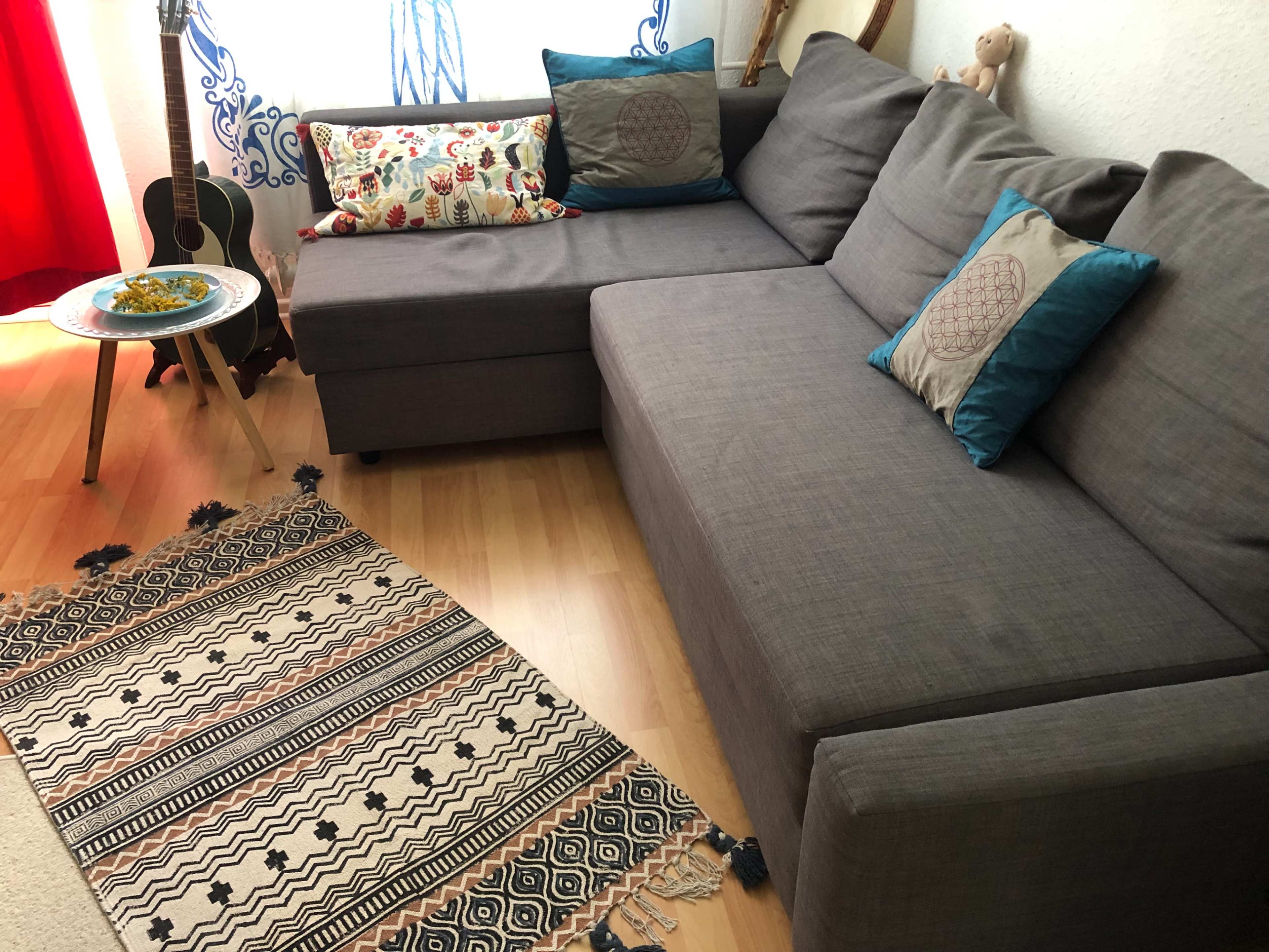 A gray sectional sofa with patterned pillows is set in a room featuring a round table, a guitar, and a decorative rug.