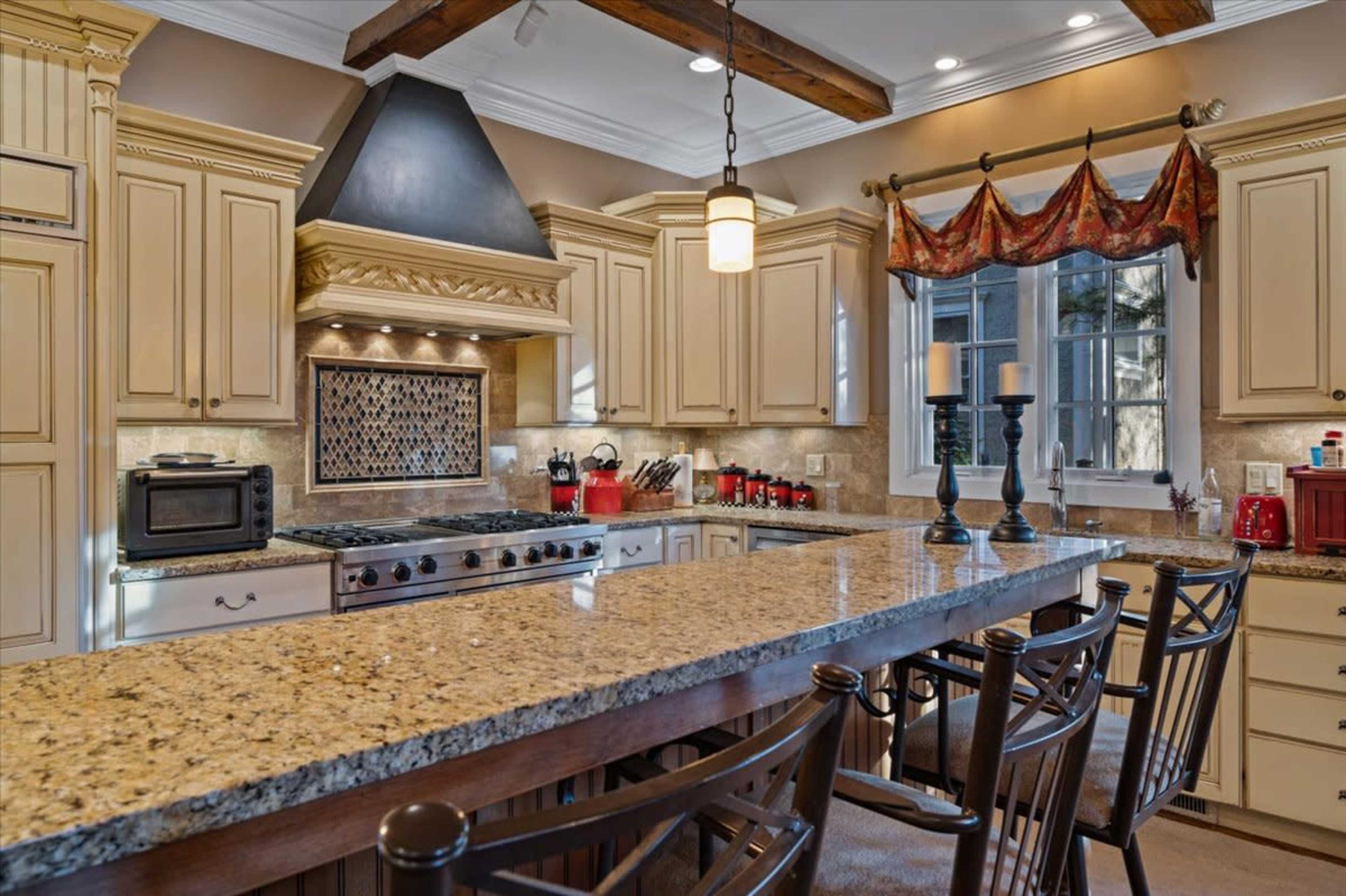 A spacious kitchen features beige cabinetry, a central island with a granite countertop, and a stainless steel range hood above a gas stove.
