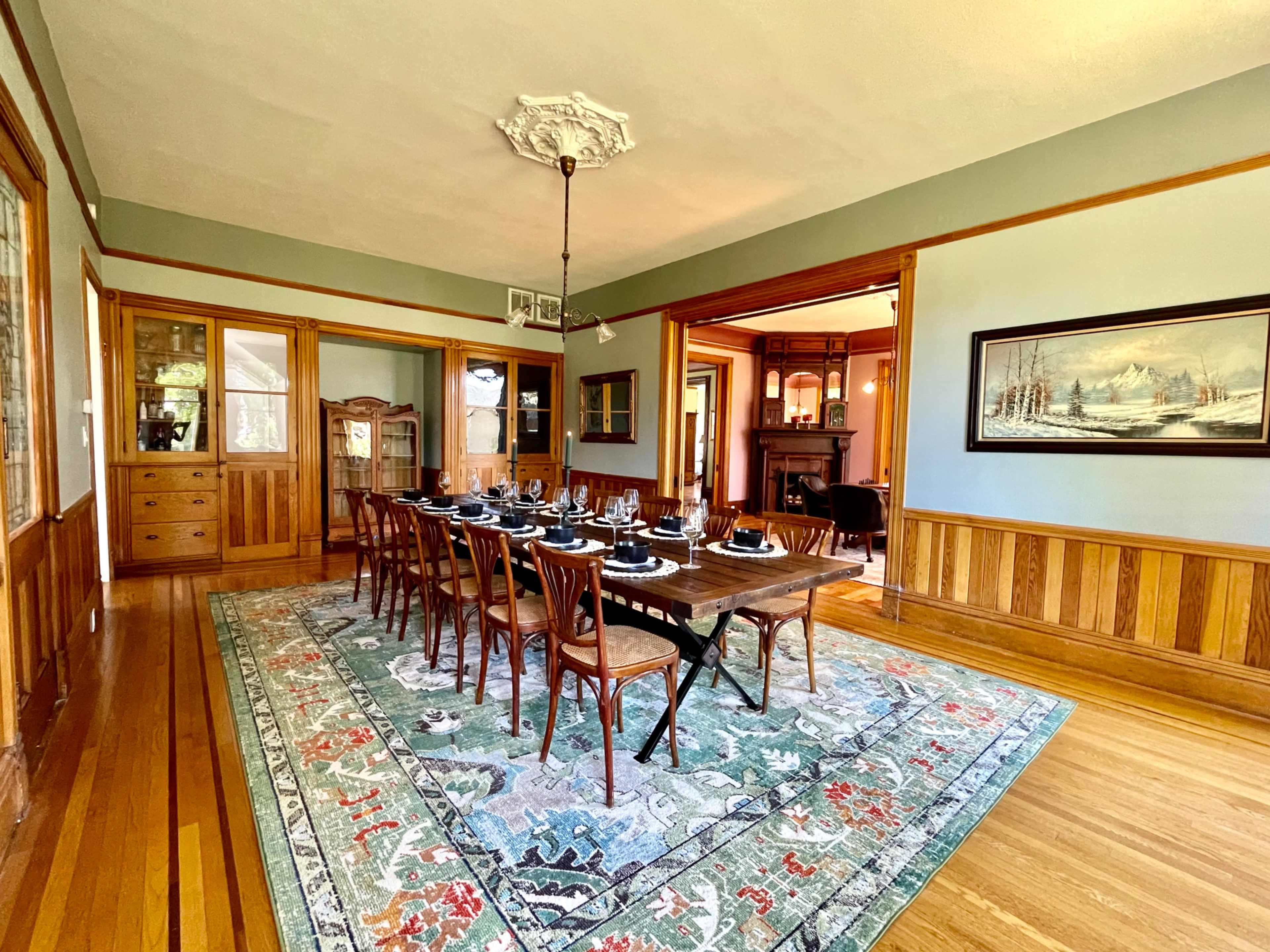 A long dining table is set for a meal in a well-furnished room with wood paneling and a decorative rug.