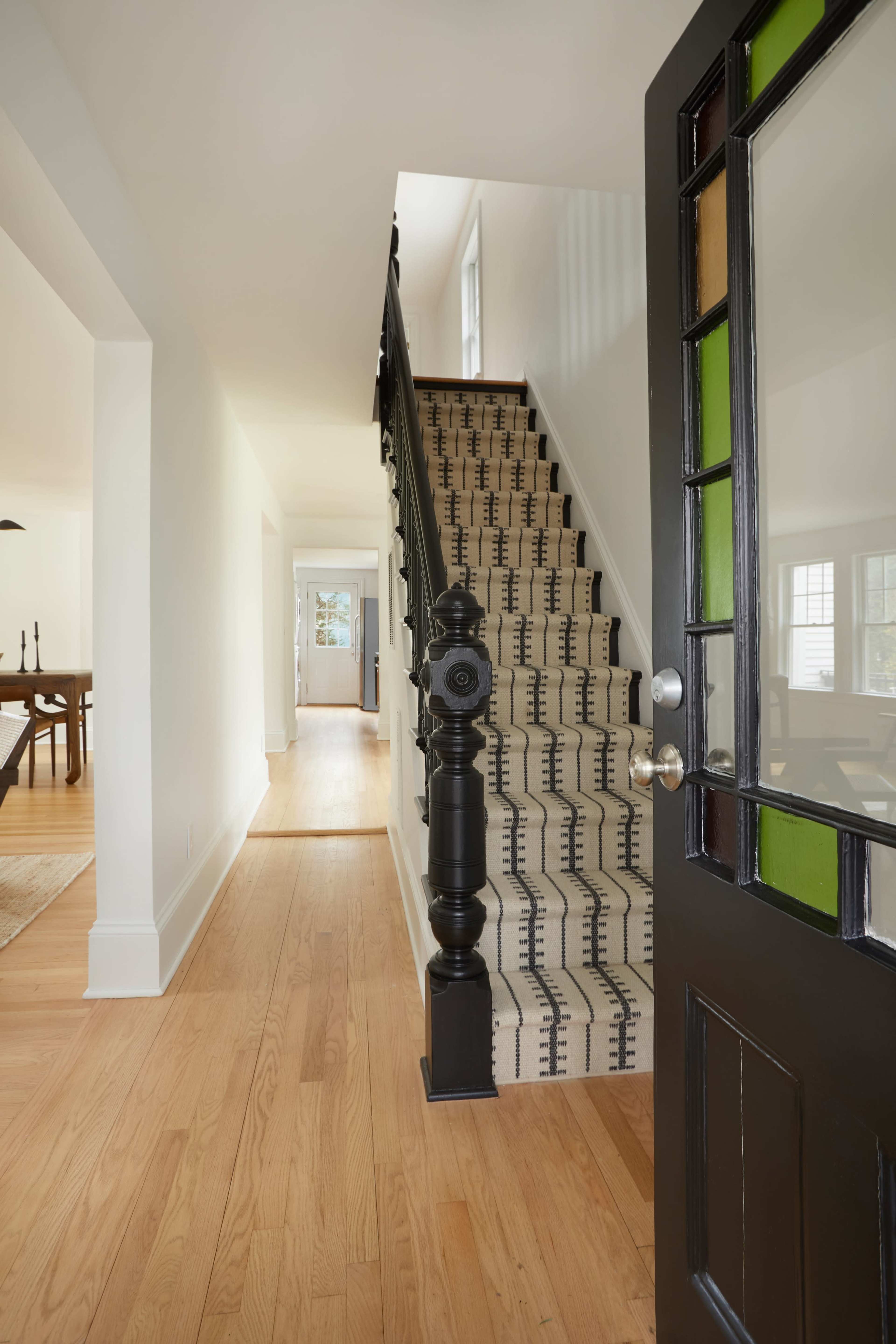 A view from an open door shows a staircase with patterned carpet leading to the upper floor of a brightly lit hallway.