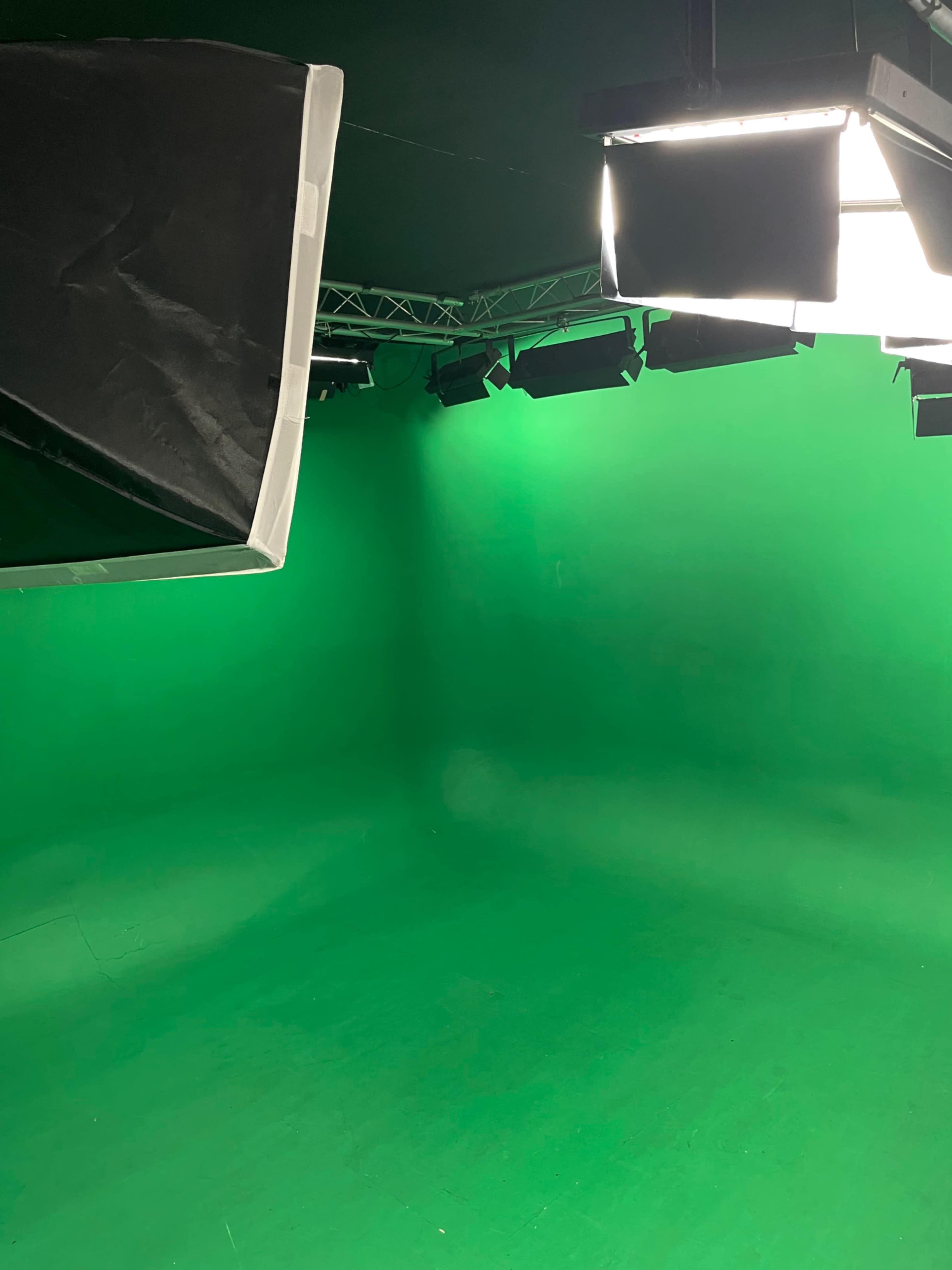 The image shows a green screen studio with lighting equipment installed on the ceiling.