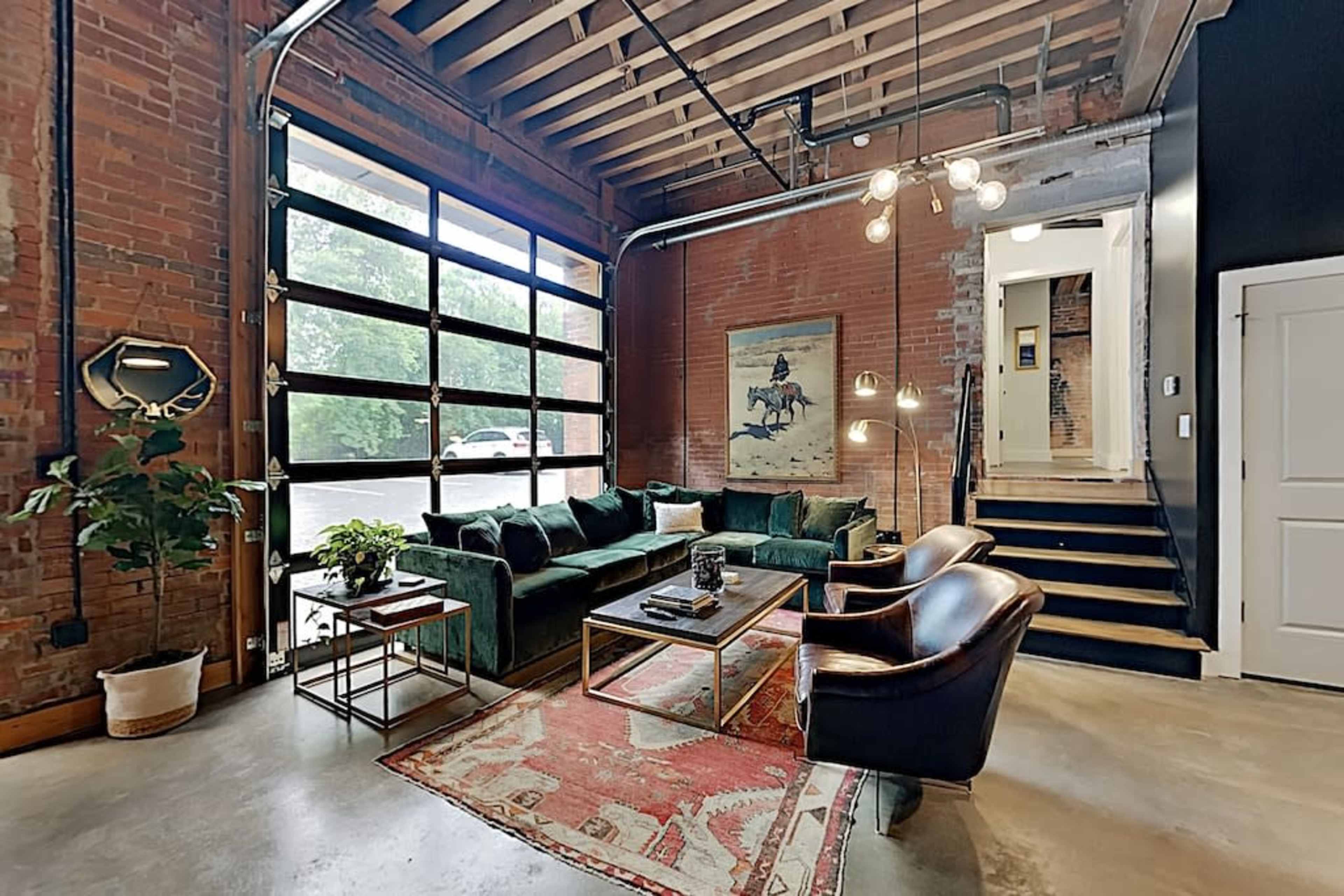 A modern living room with a green velvet sofa, a wooden coffee table, and an open garage-style door that allows natural light into the space.