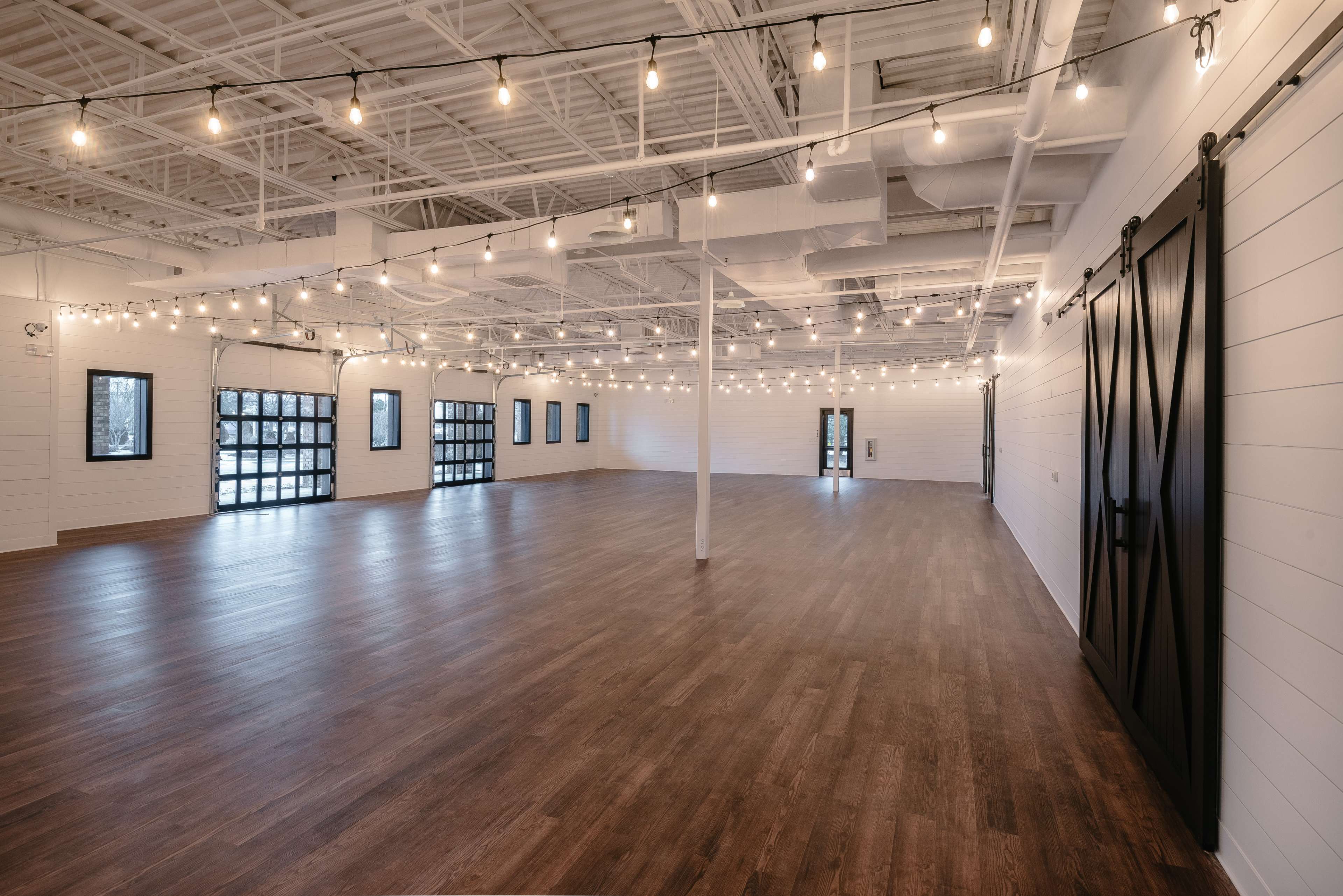 A spacious, empty room with wooden floors and string lights hanging from the ceiling.
