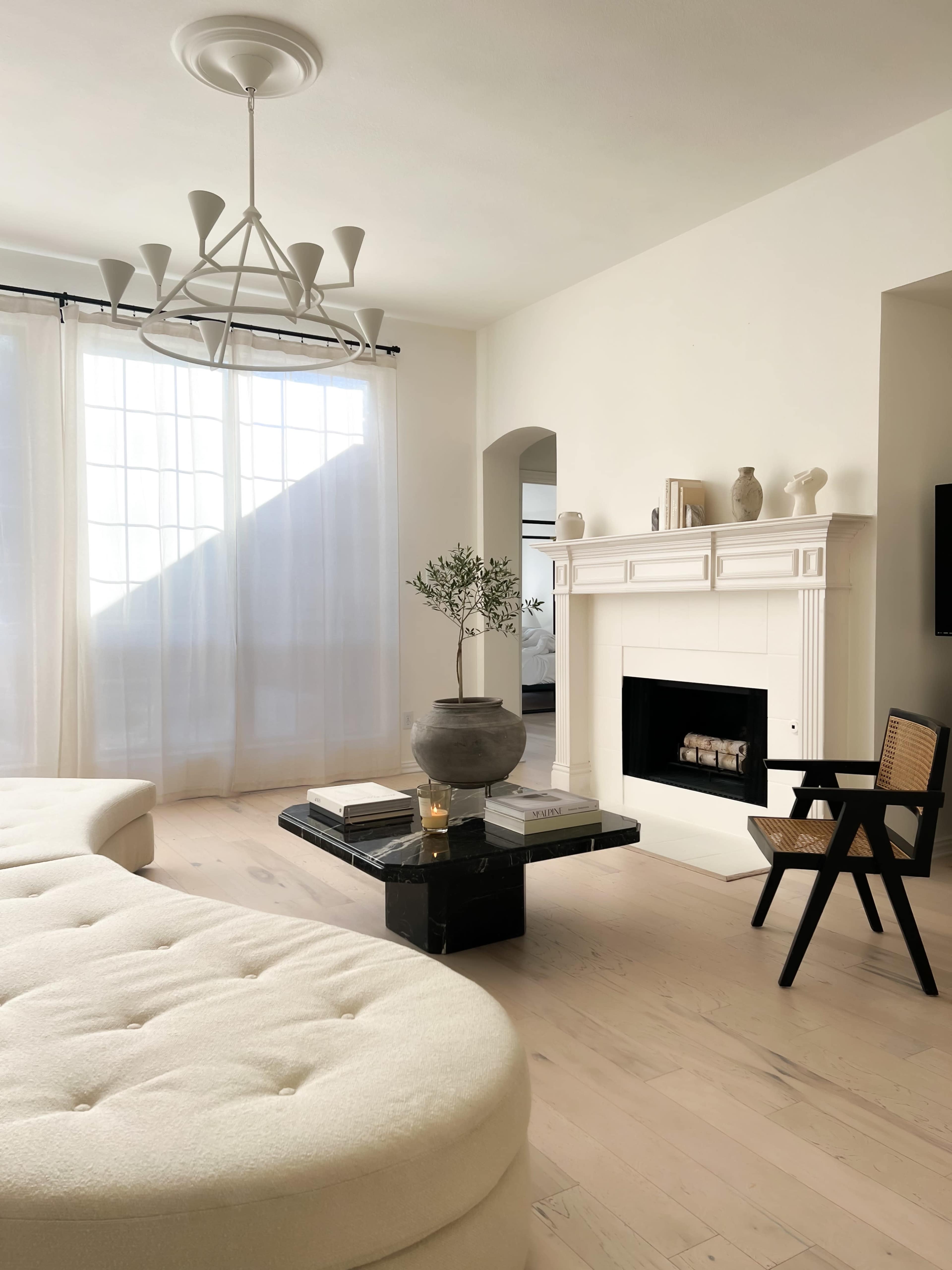 The scene features a modern living room with a large white sofa, a minimalist fireplace, a black coffee table, and a decorative chair.
