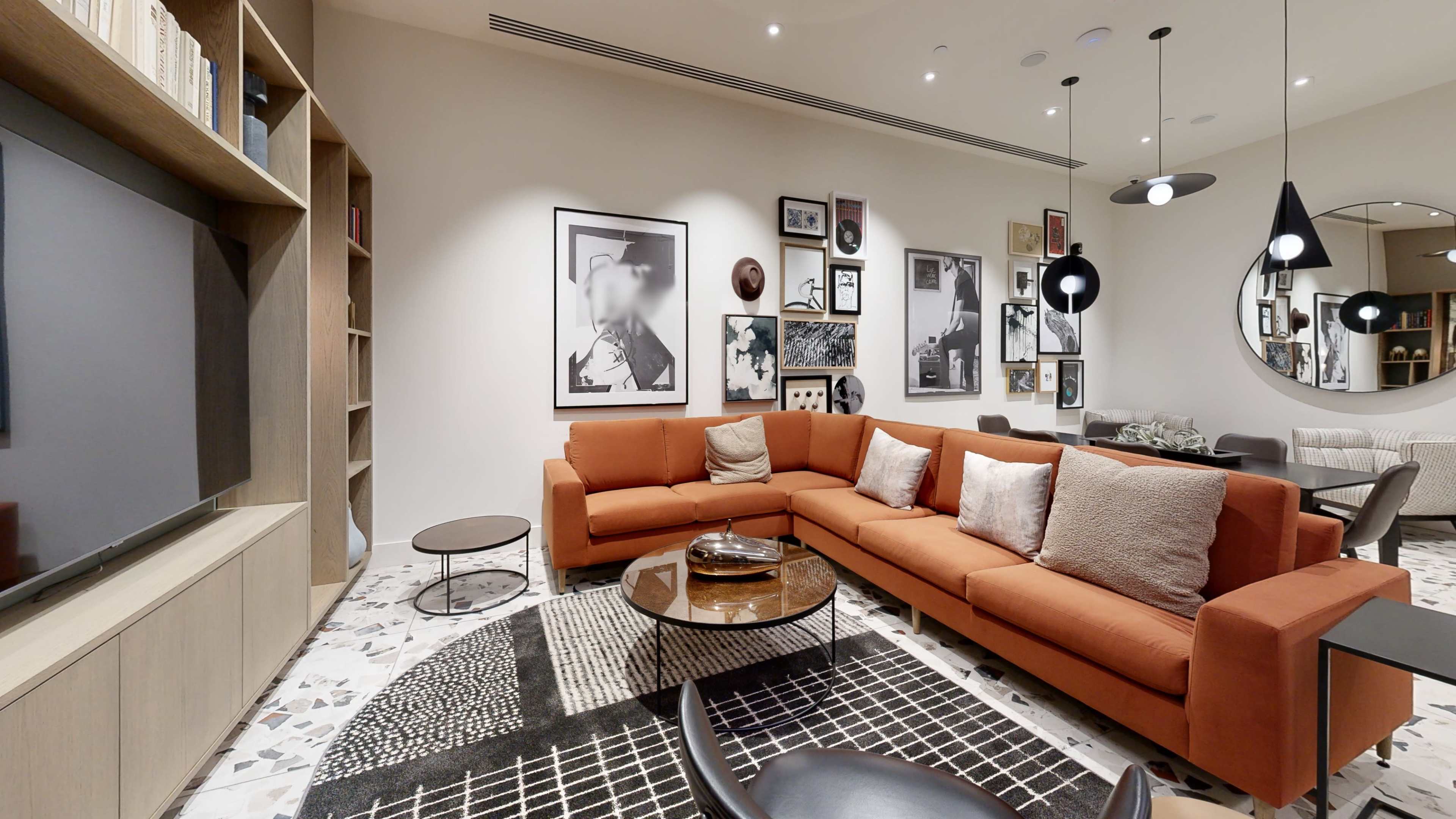 A modern living room with an orange sectional sofa, a round coffee table, framed art on the walls, and a decorative rug.