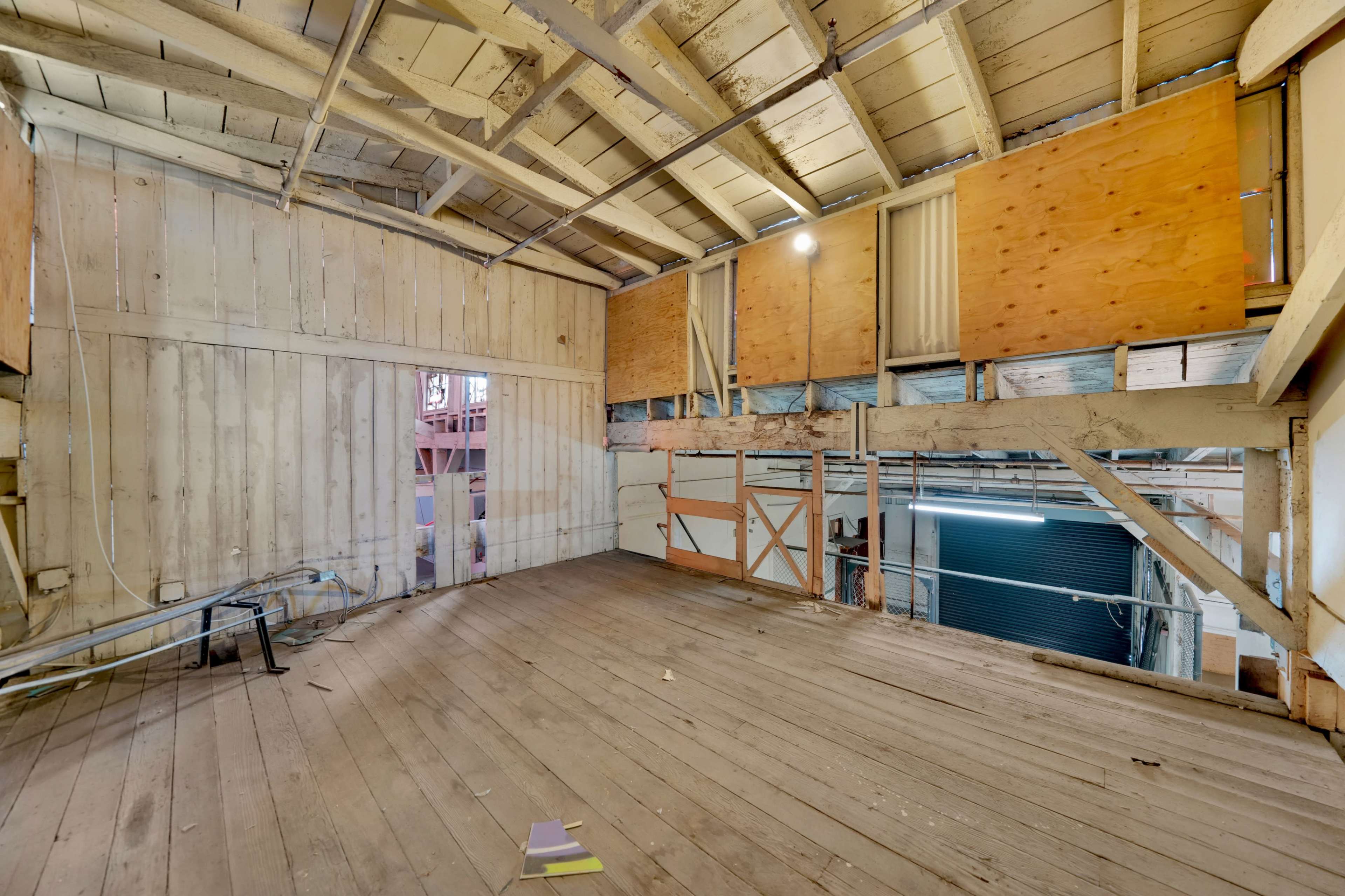 An unfinished wooden interior of a loft space with exposed beams and walls partially covered by plywood.