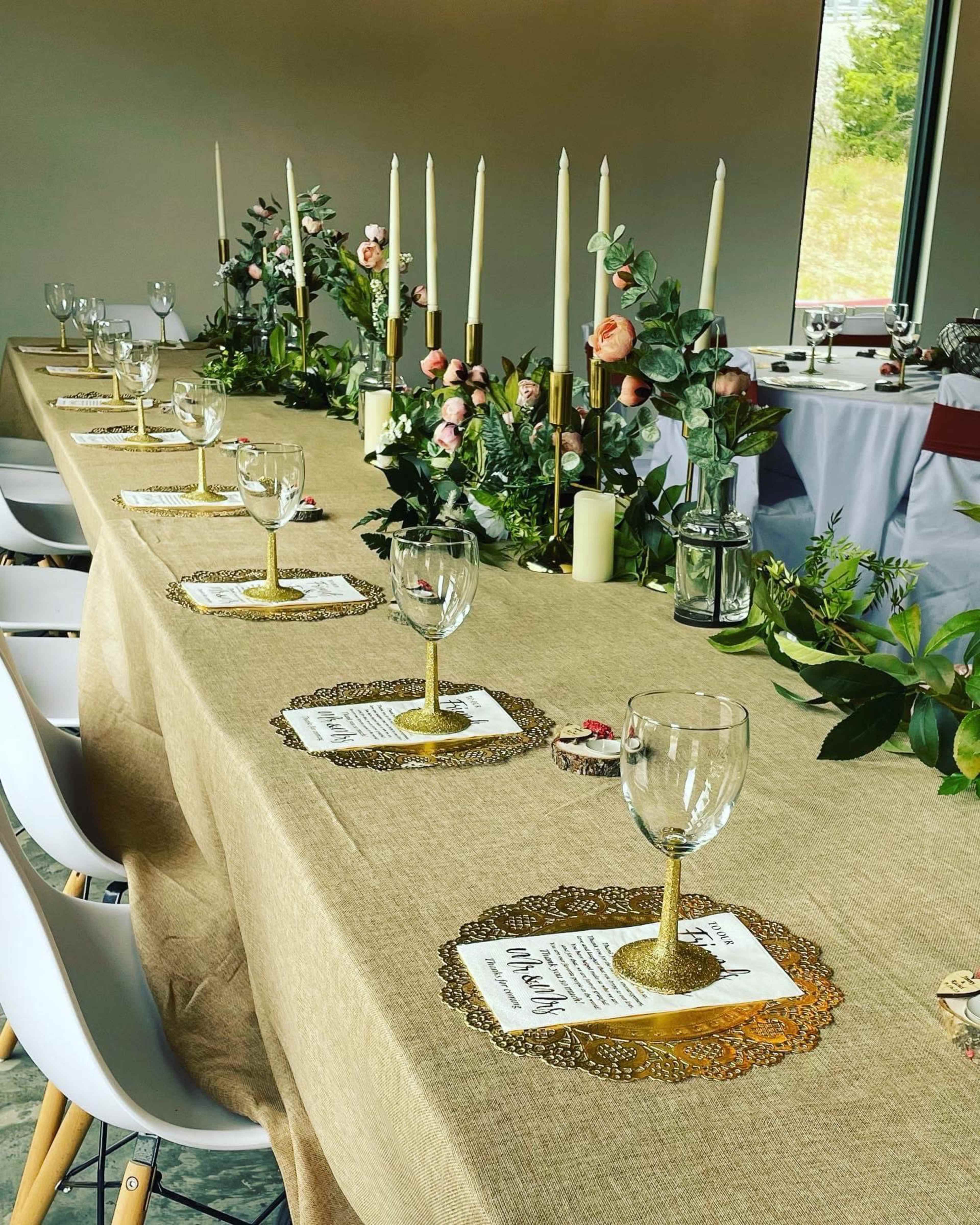 A long table is elegantly set with floral centerpieces, candles, and gold-accented glassware in a bright room.