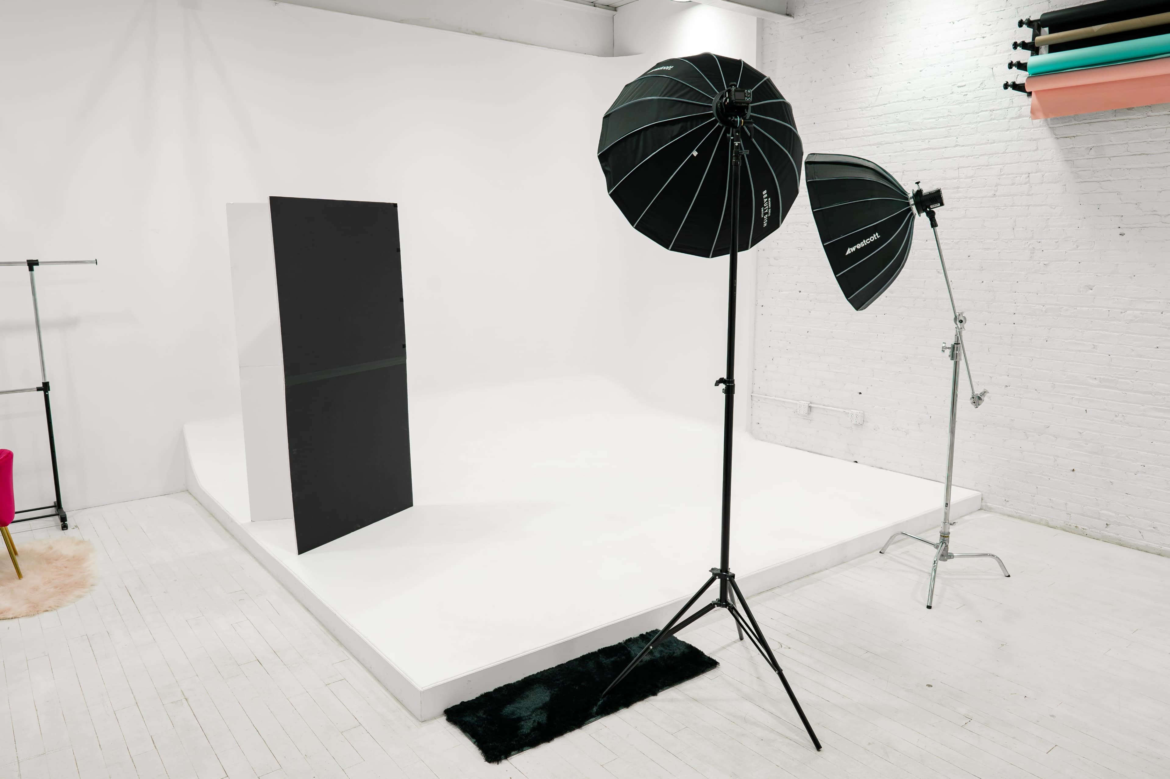 A photography studio with a white backdrop, two light stands with softboxes, and a black fabric divider on the set.