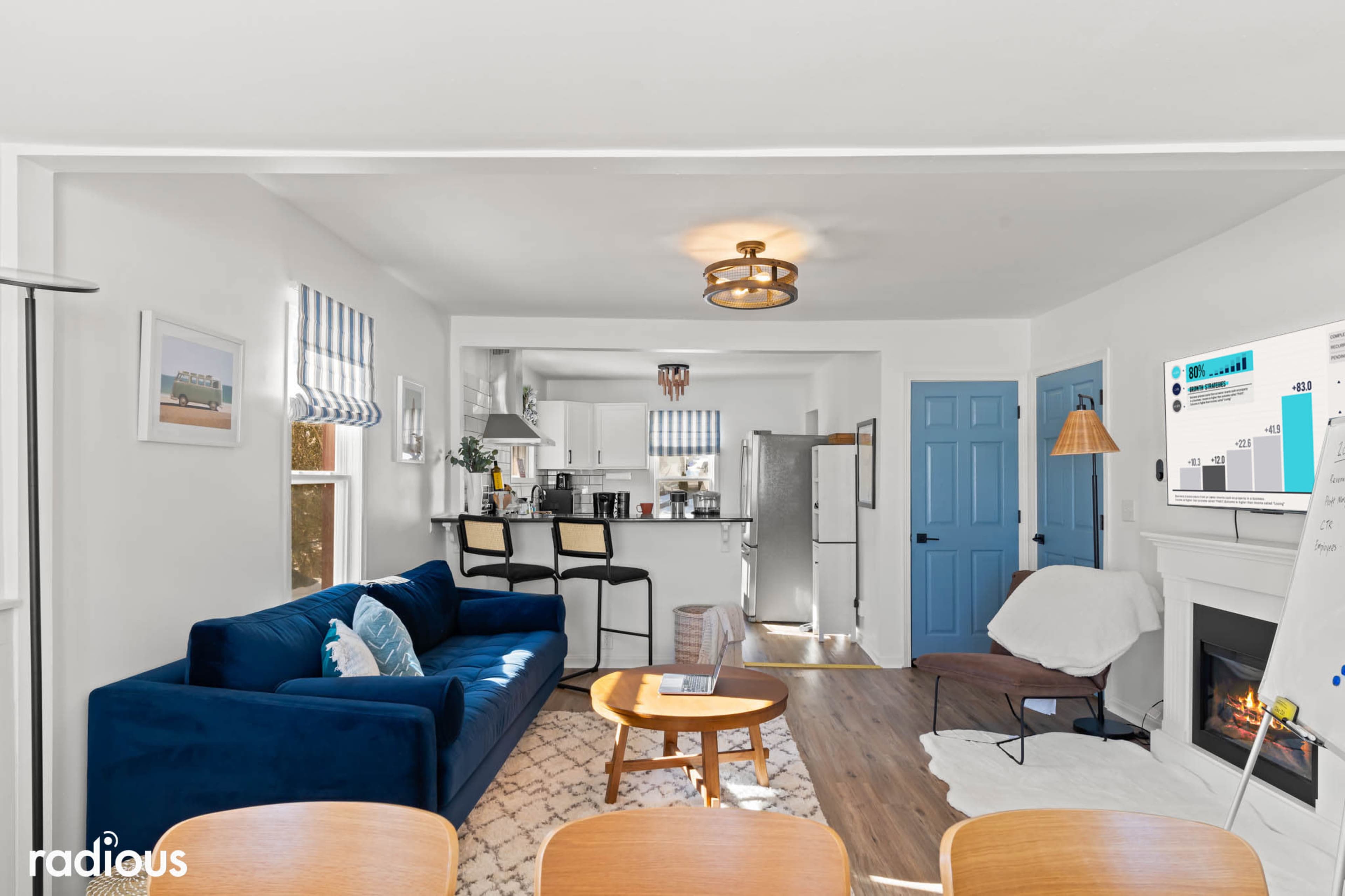A modern living room with a blue sofa, a dining area with wooden chairs, and an open kitchen in the background.