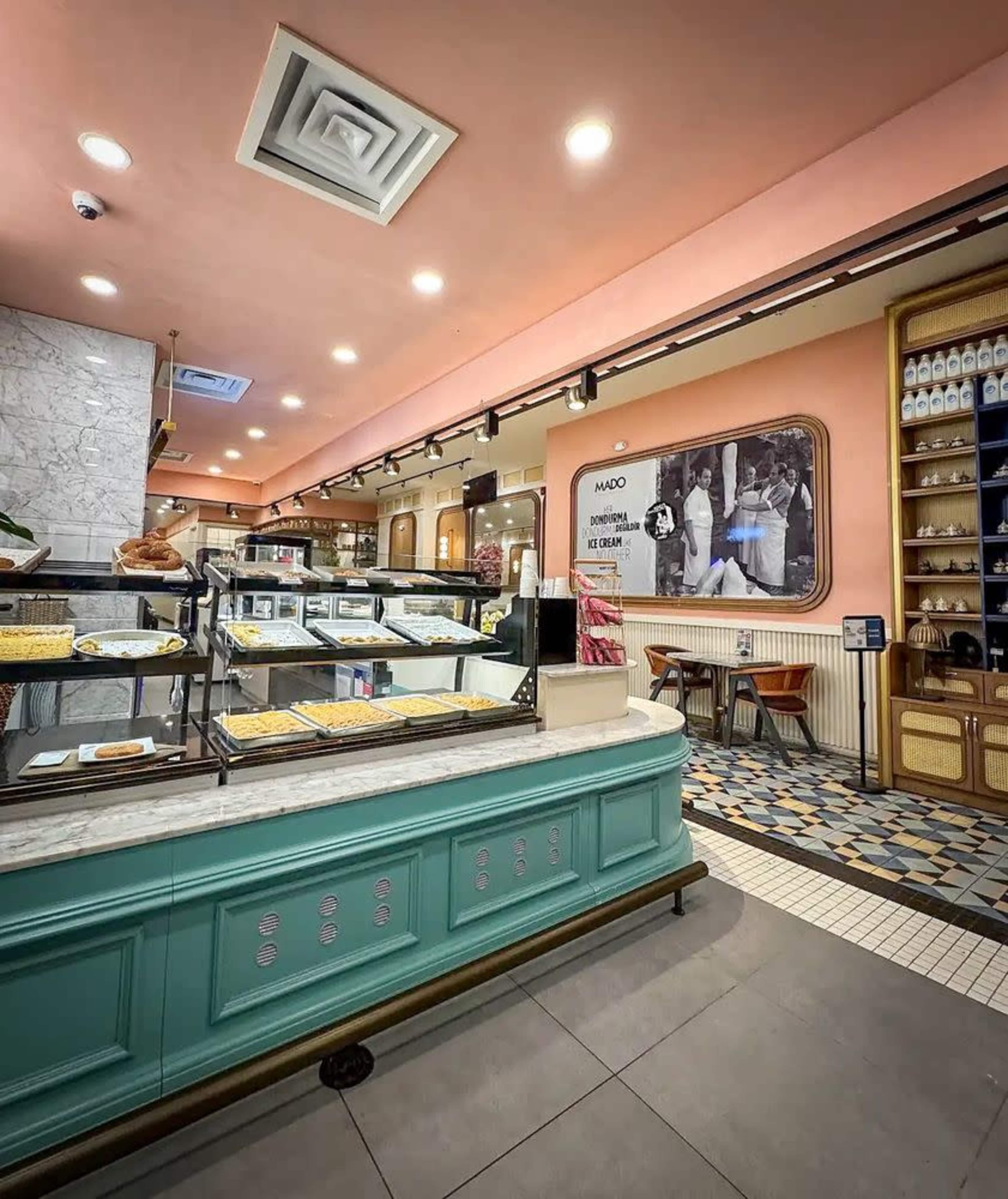 The image shows the interior of a café, featuring a display counter with pastries and a brightly colored wall, illuminated by overhead lights.
