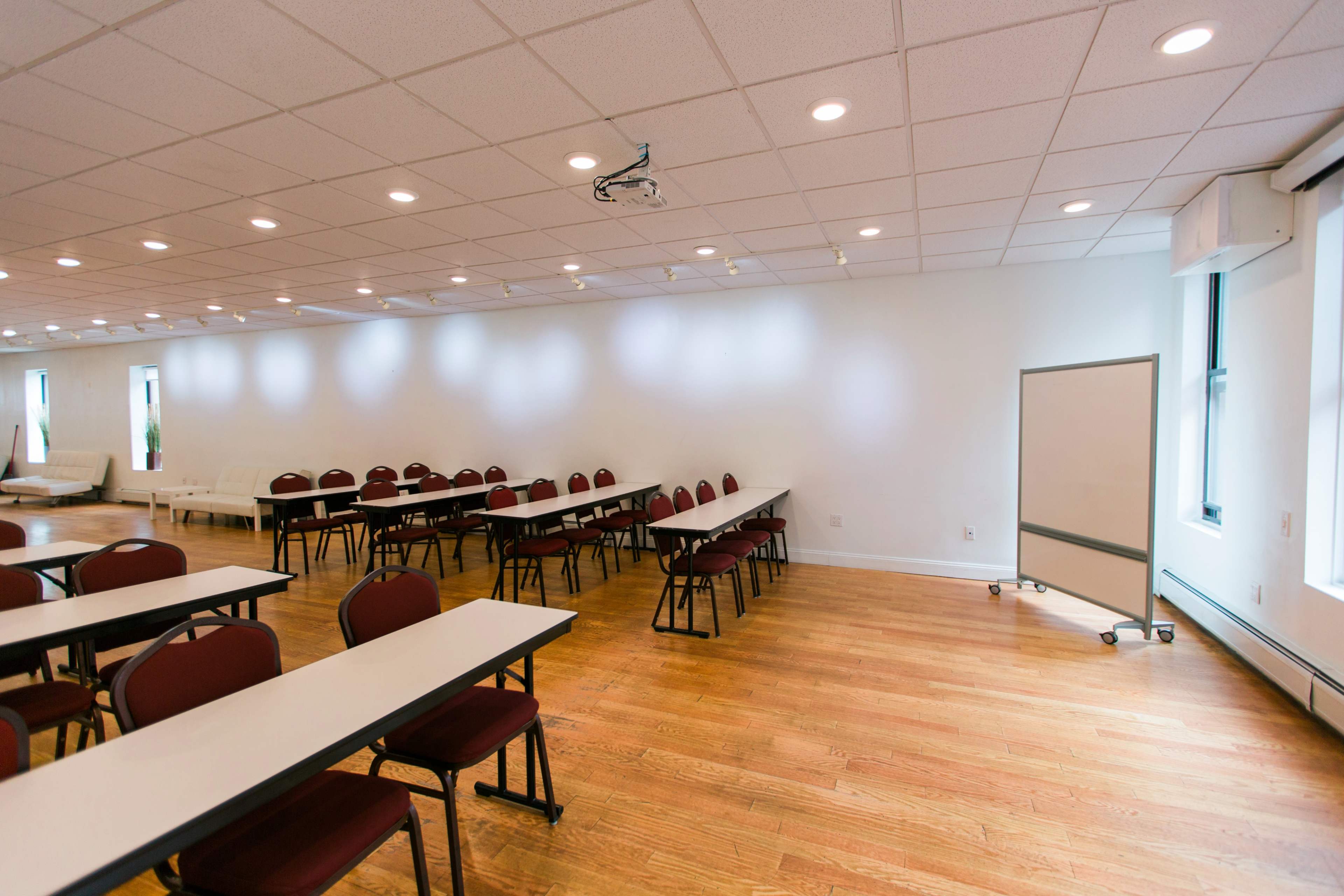 A spacious, well-lit meeting room with several tables and chairs arranged in rows and a whiteboard in the corner.