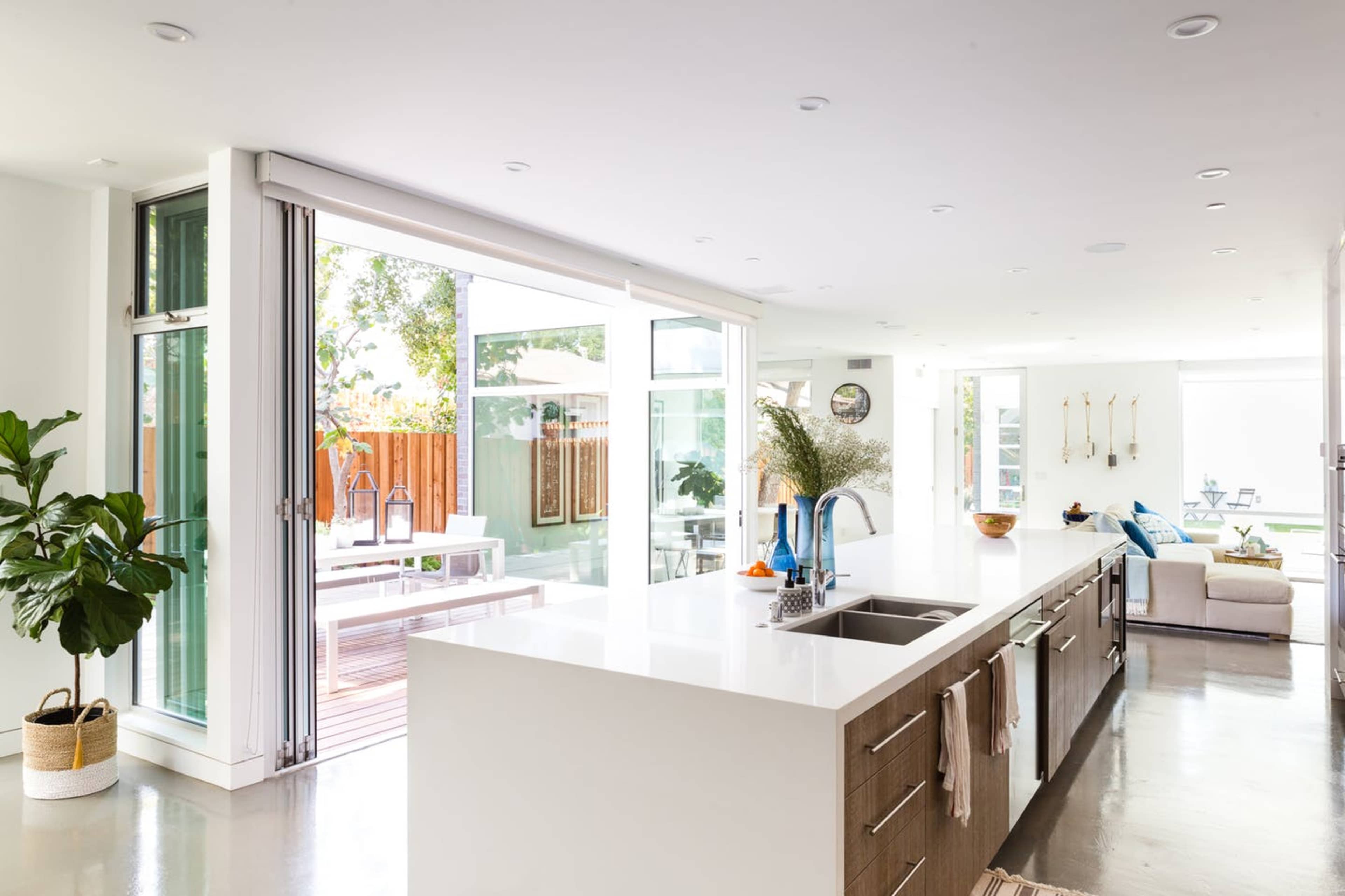 A modern kitchen with a large island, featuring open sliding glass doors that lead to an outdoor patio area.