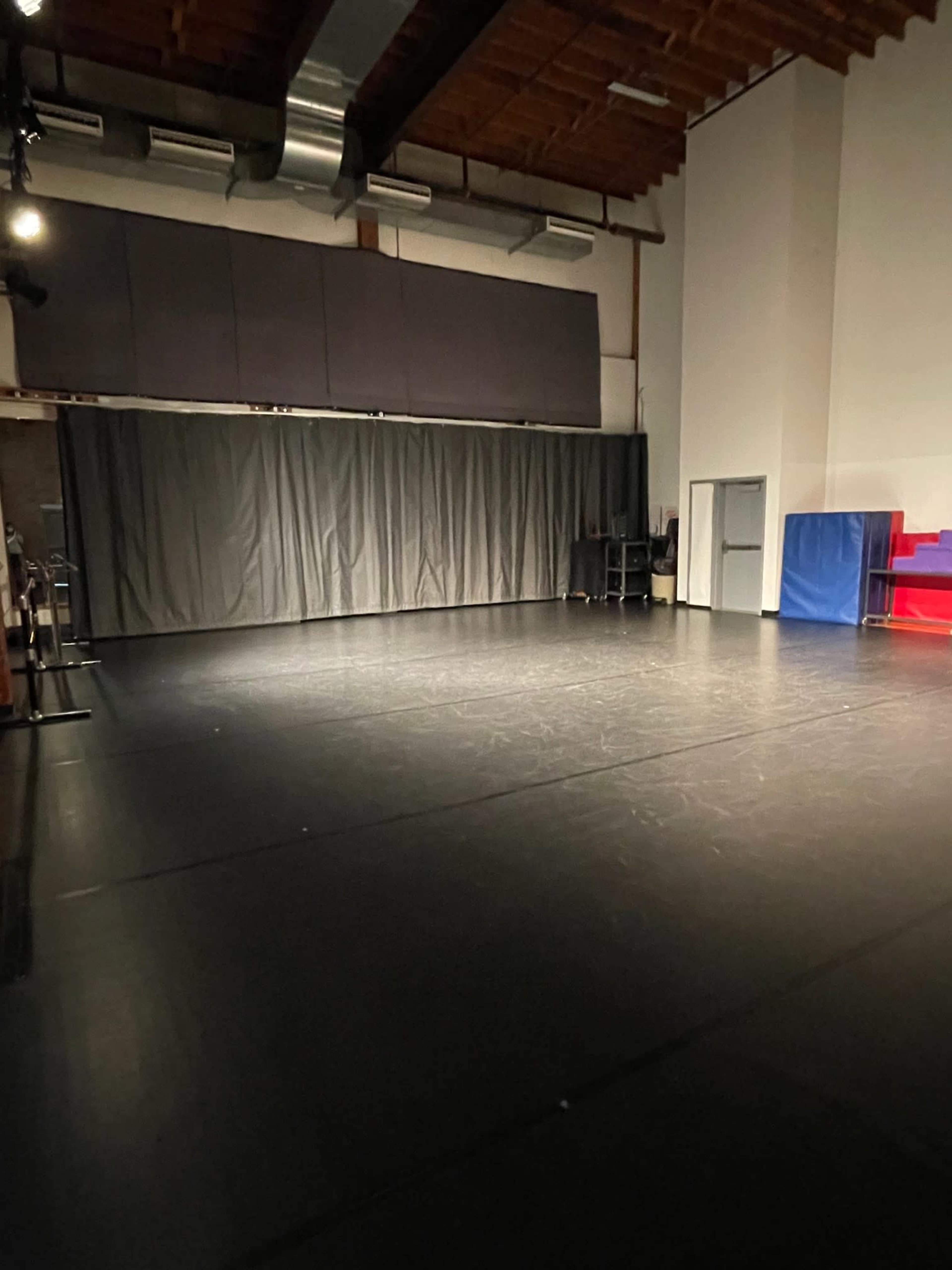 A spacious, darkly lit studio with a black floor, gray curtains, and some equipment along the walls.