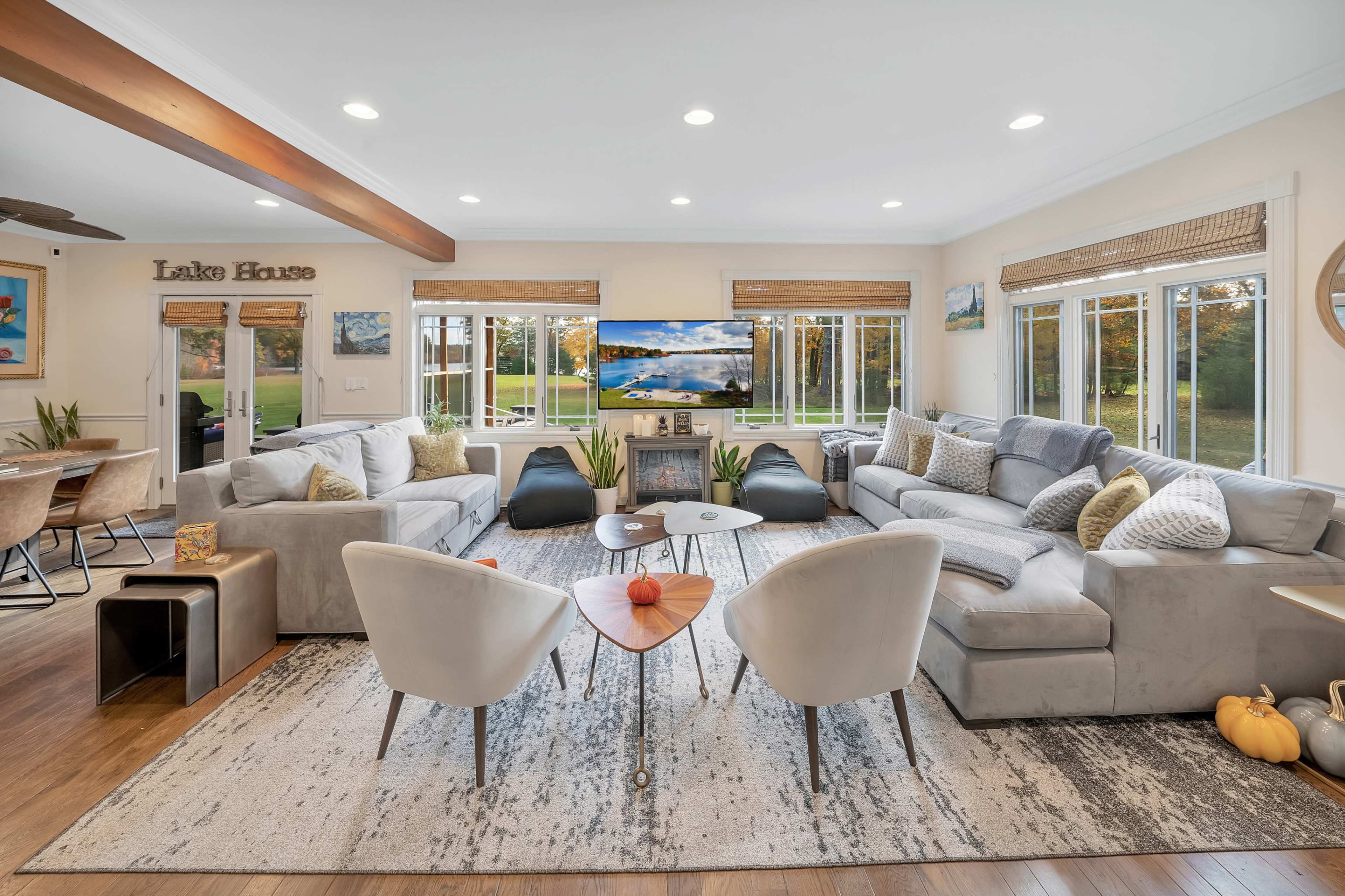 A spacious living room features a sectional sofa, two accent chairs, and a large TV, with windows providing a view of the outside.