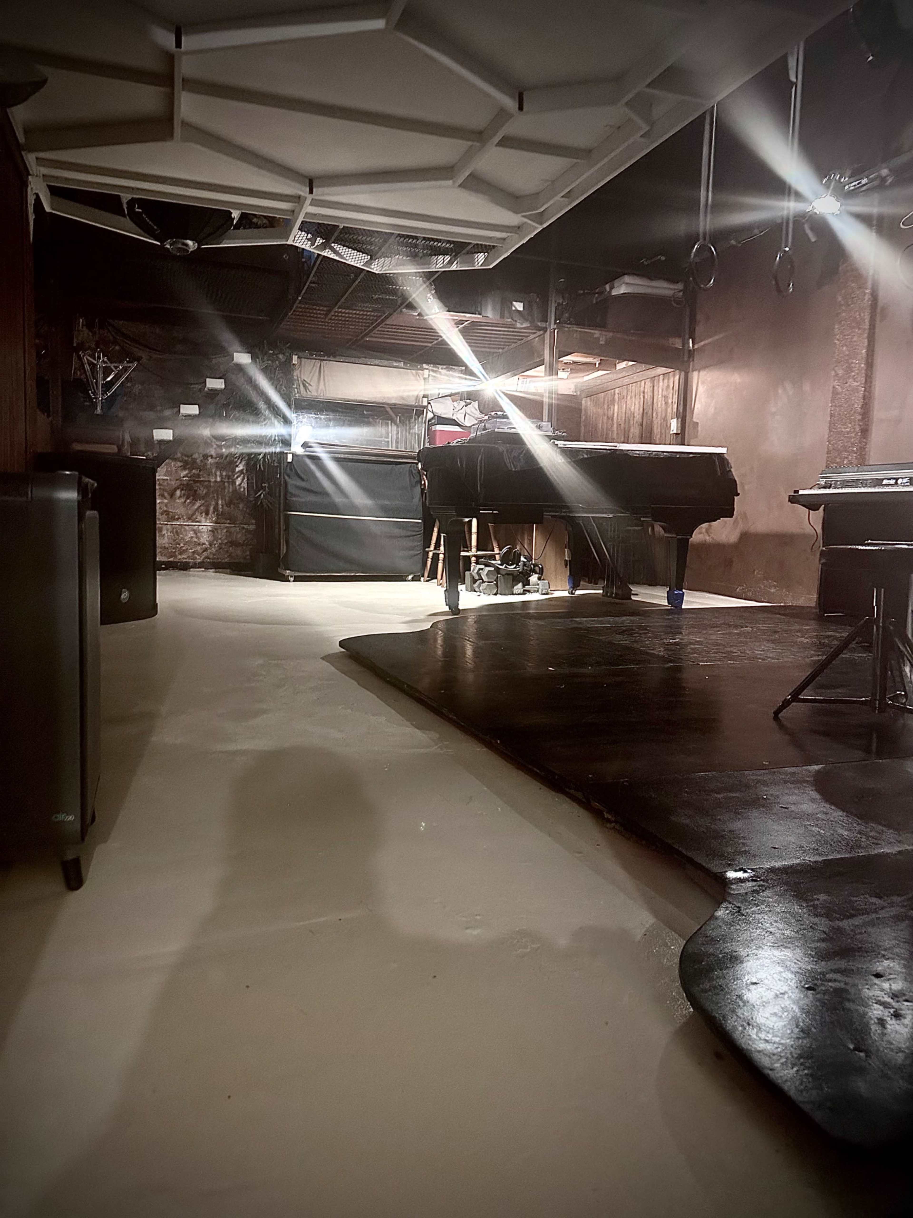 The image shows a dimly lit basement space with a smooth floor, dark furniture, and a variety of equipment arranged throughout the area.