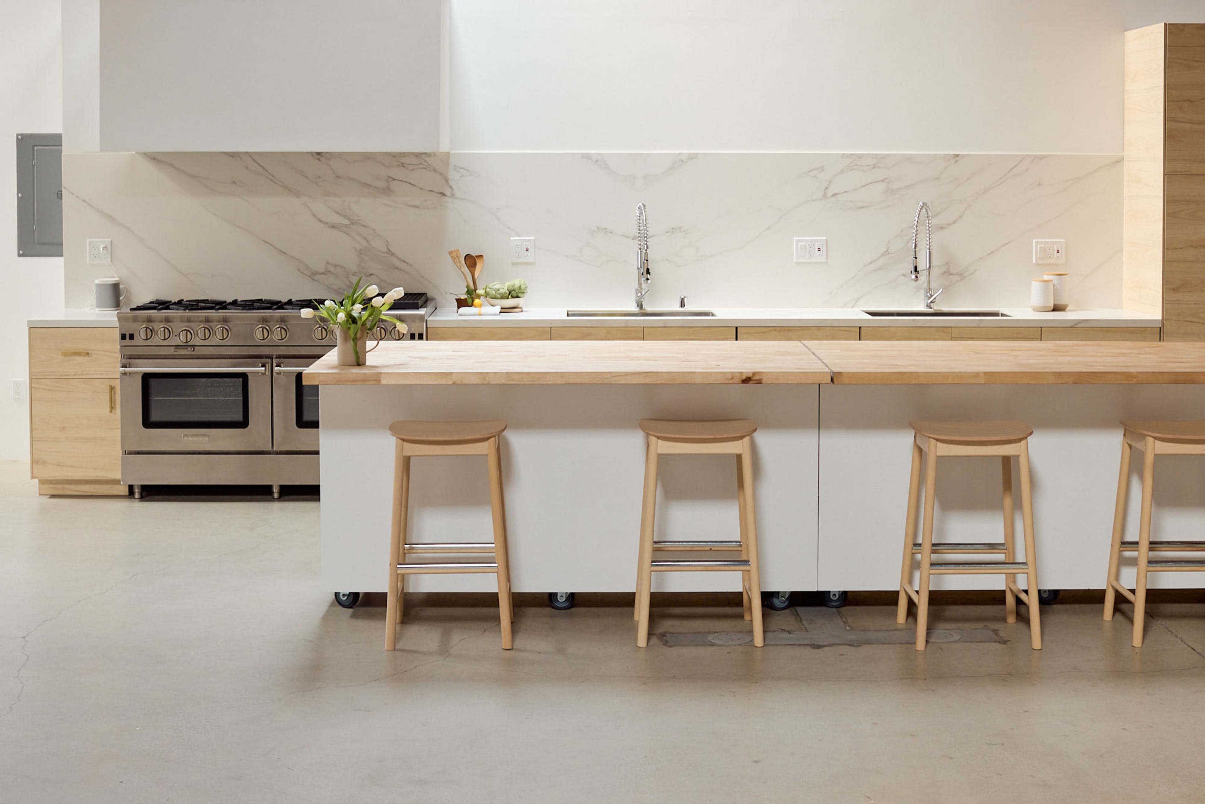 A modern kitchen features a wooden island with stools, stainless steel appliances, and a marble backsplash.