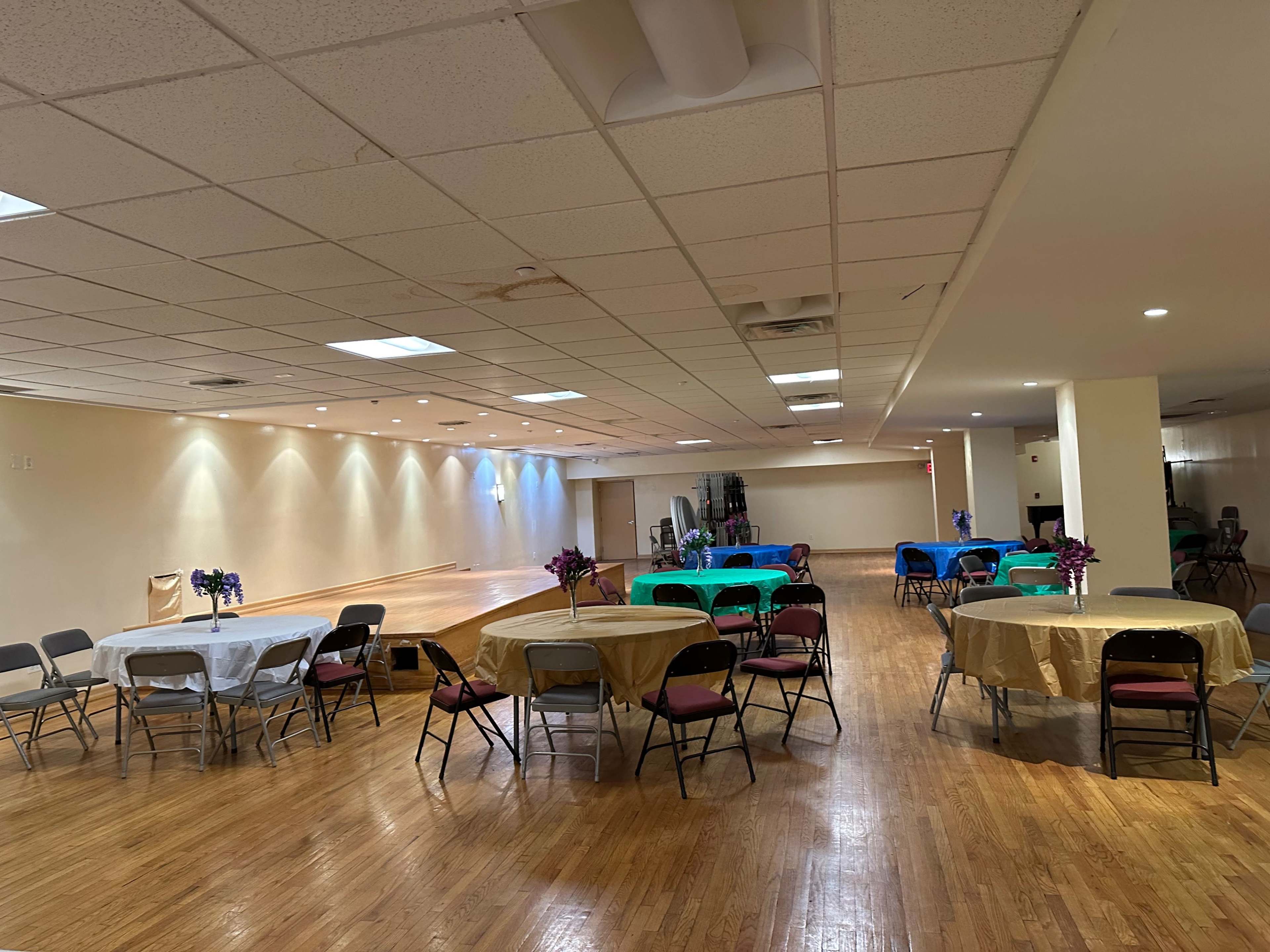 An indoor event space with several round tables set up, each decorated with tablecloths and floral arrangements.
