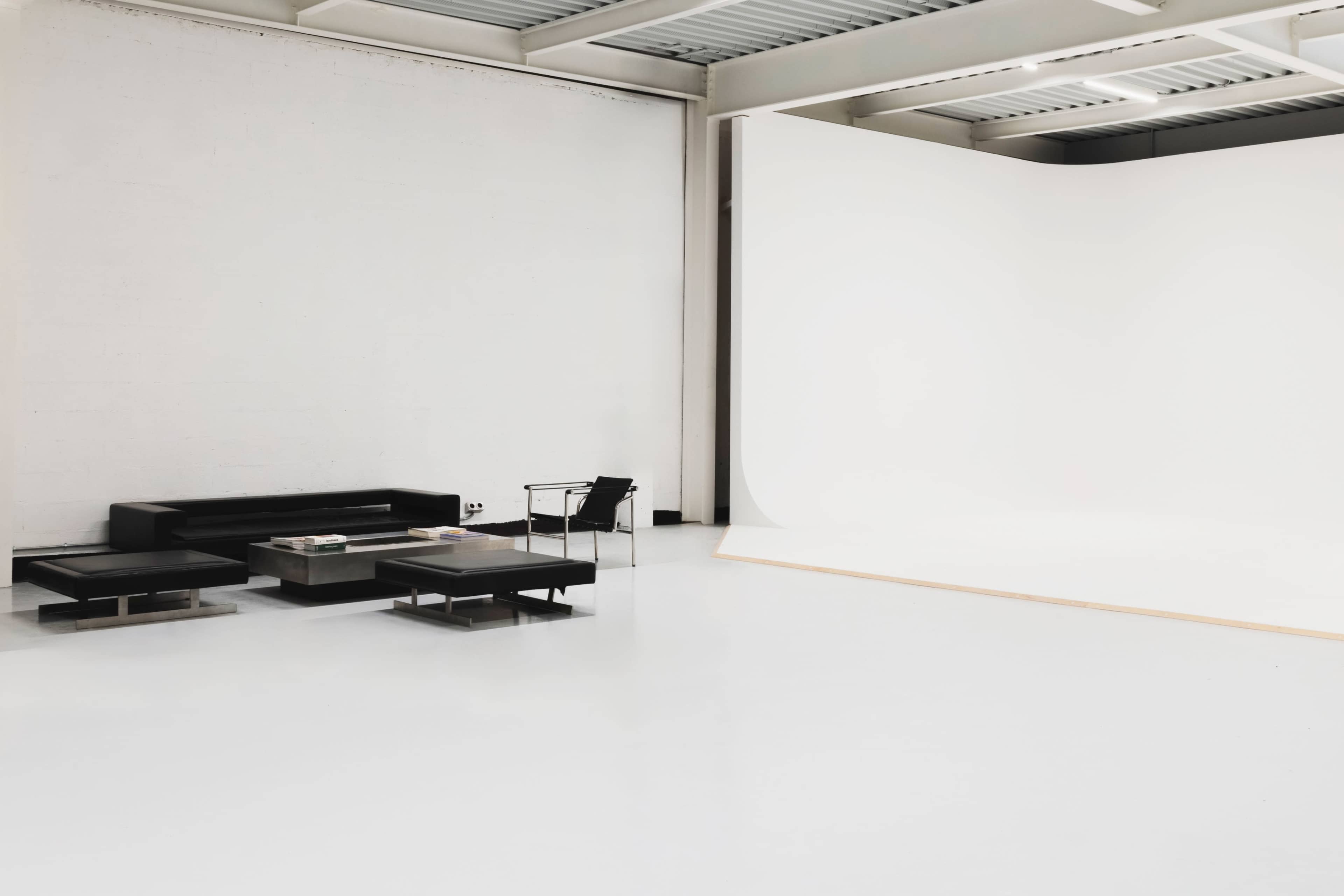 A modern, minimalist studio features a black sofa, a glass coffee table, and a large white backdrop.