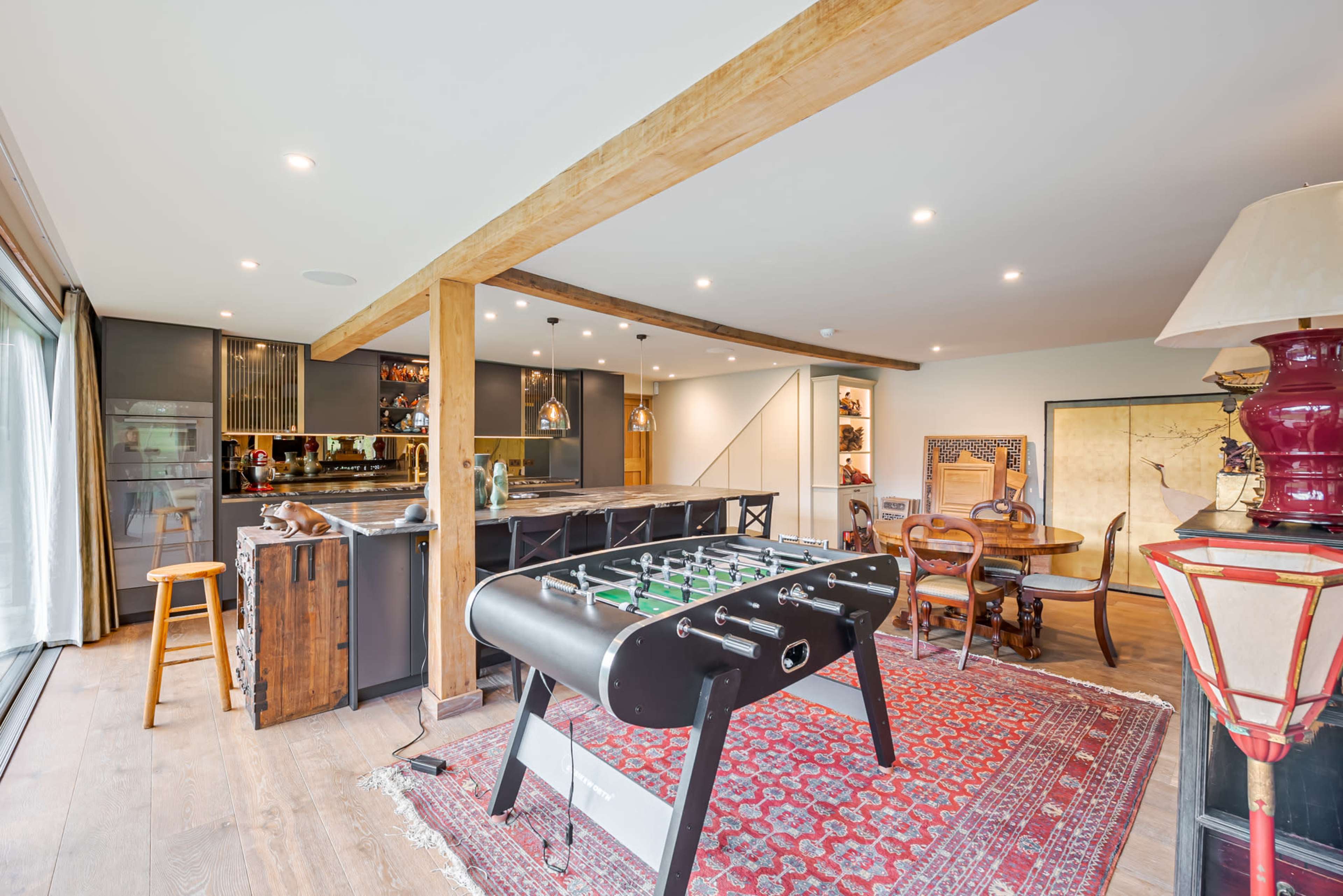 The image shows a modern kitchen and dining area featuring a foosball table, wooden beams, and a mix of contemporary and vintage furniture.