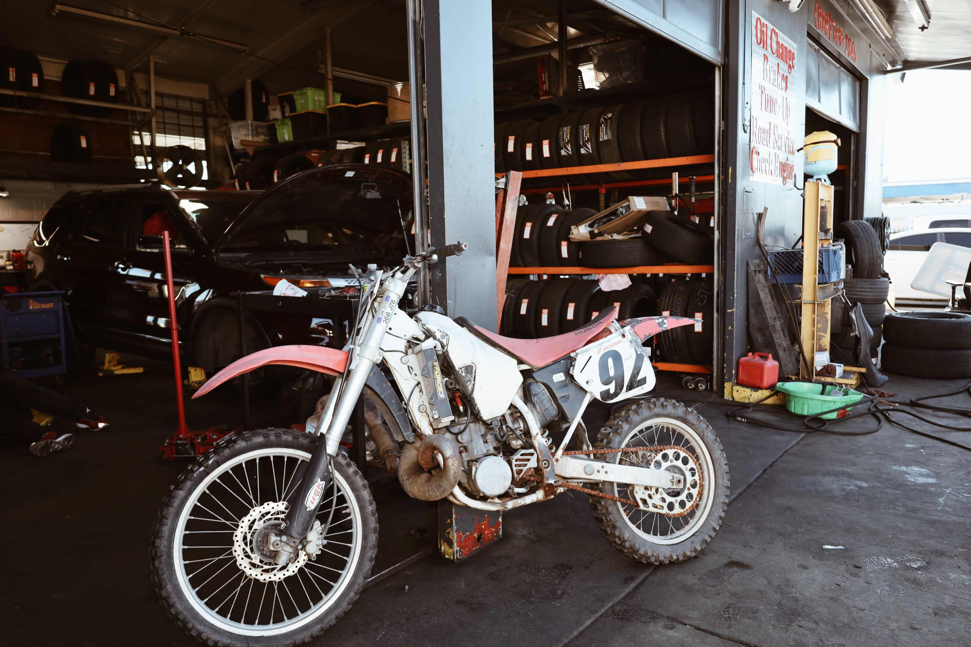 A dirt bike with the number 94 is parked in a garage filled with tires and various automotive tools.