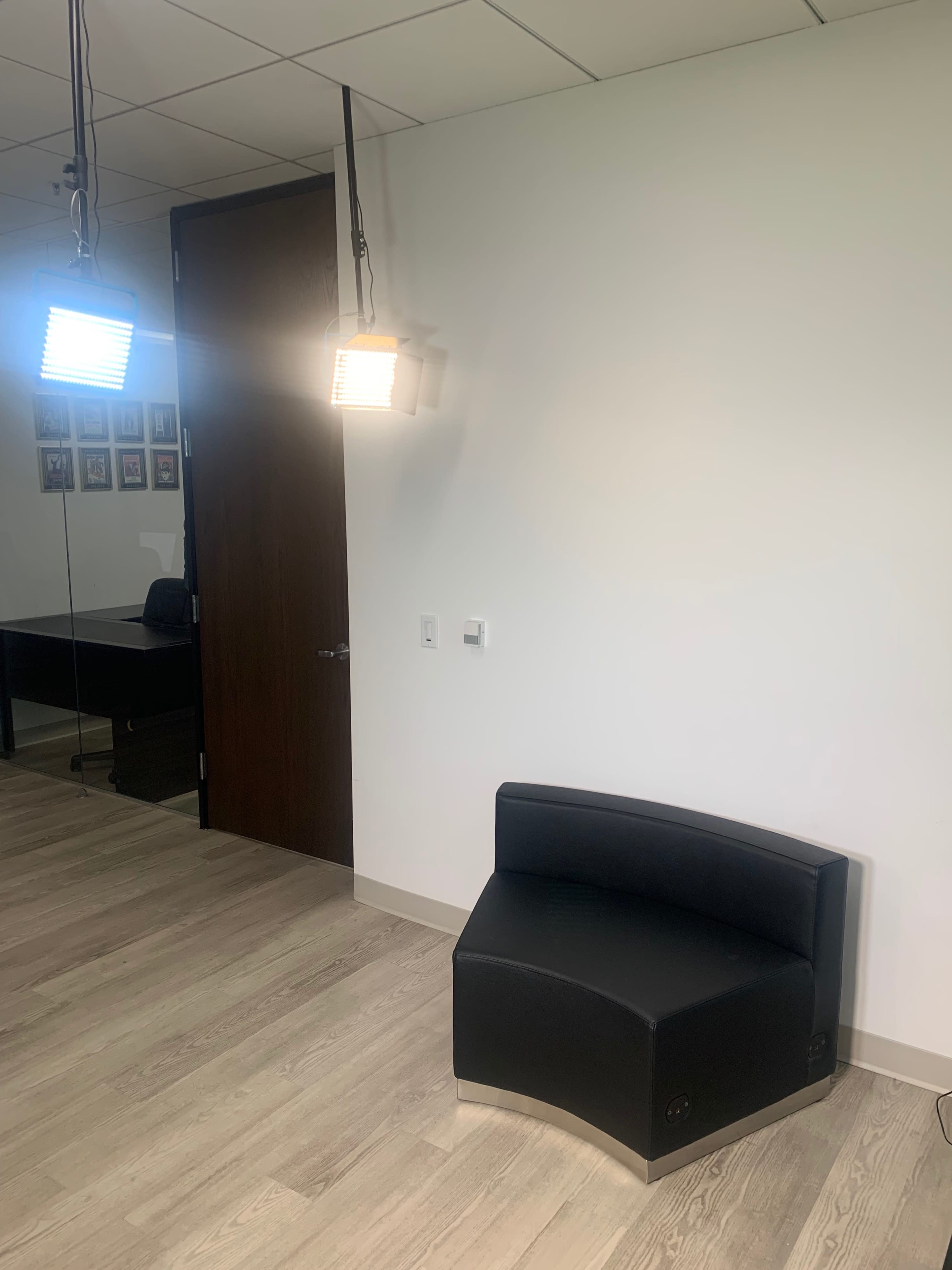 A simple office space featuring a black curved bench, two pendant lights, and a door leading to another room with framed pictures on the wall.