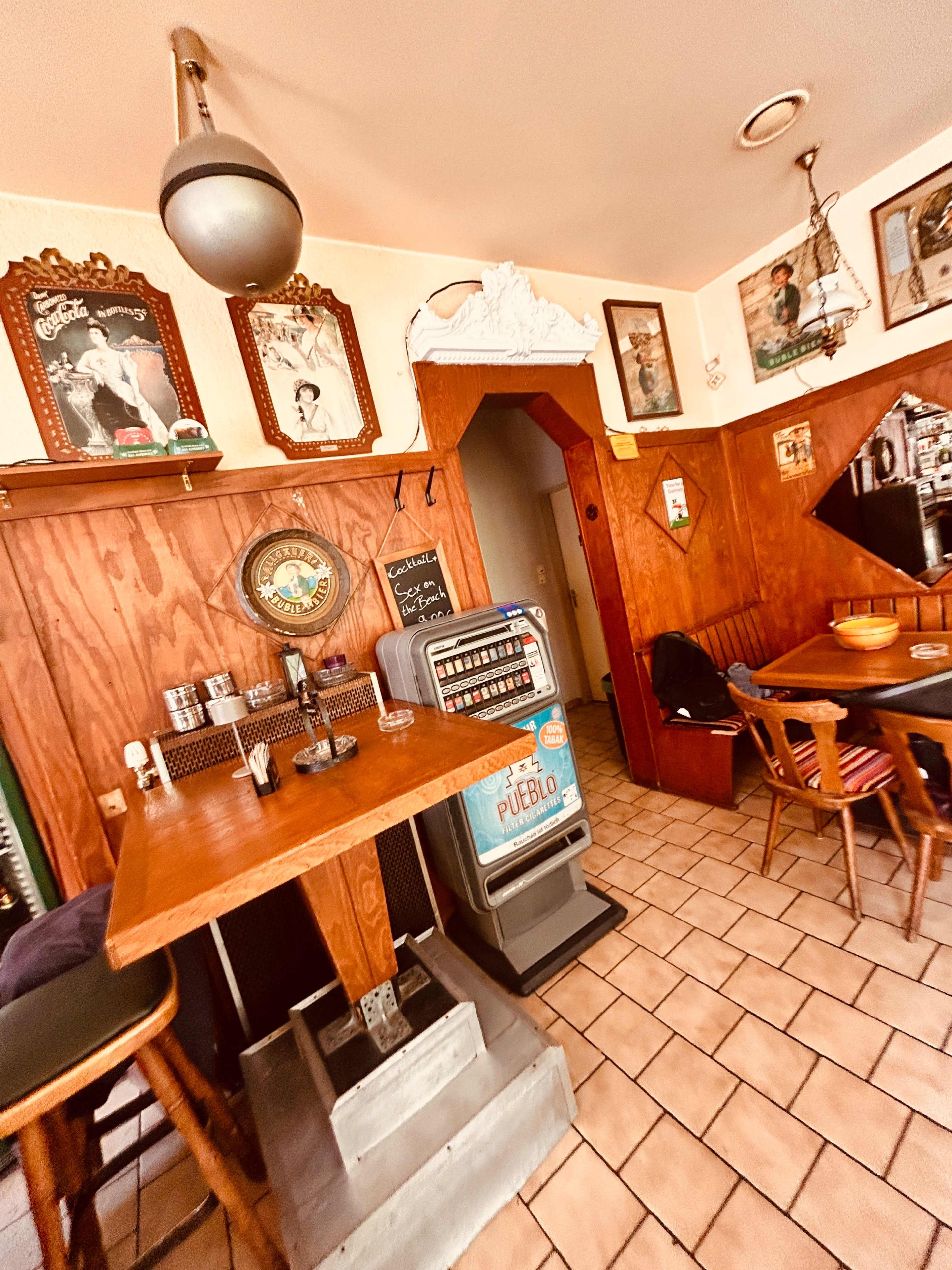 The image shows a cozy, rustic interior of a small café or bar with wooden walls, a wooden table, and vintage decor.