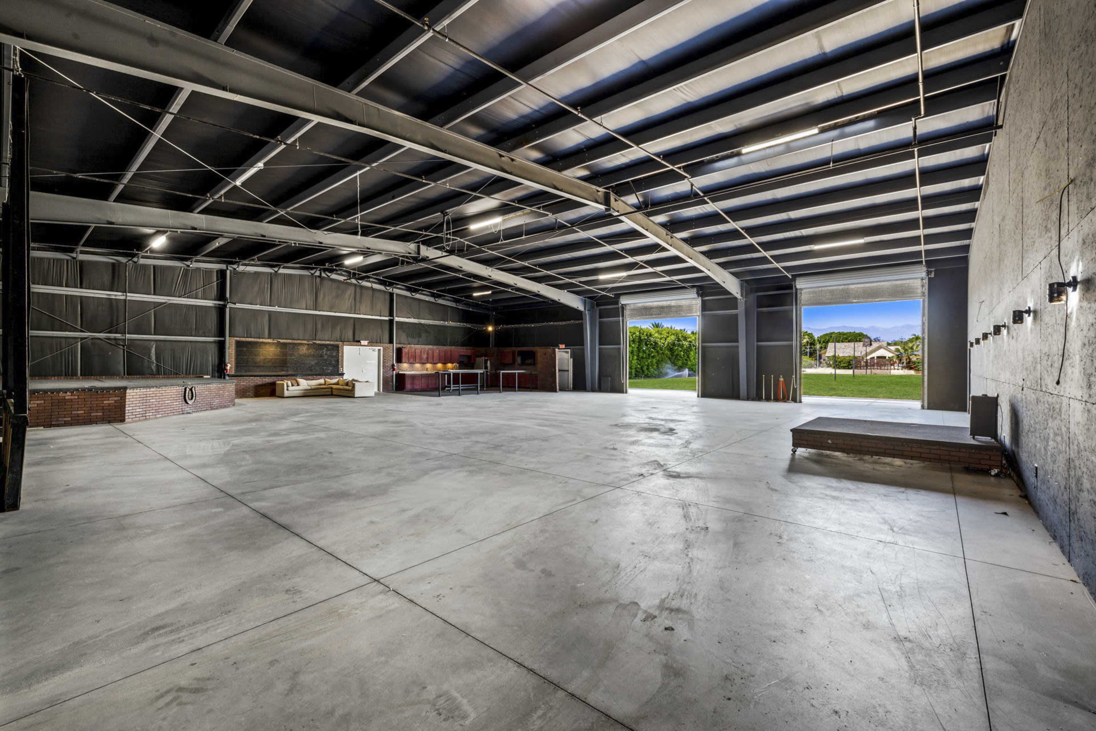 A spacious, empty industrial garage with a concrete floor and large open doors leading to an outdoor area.