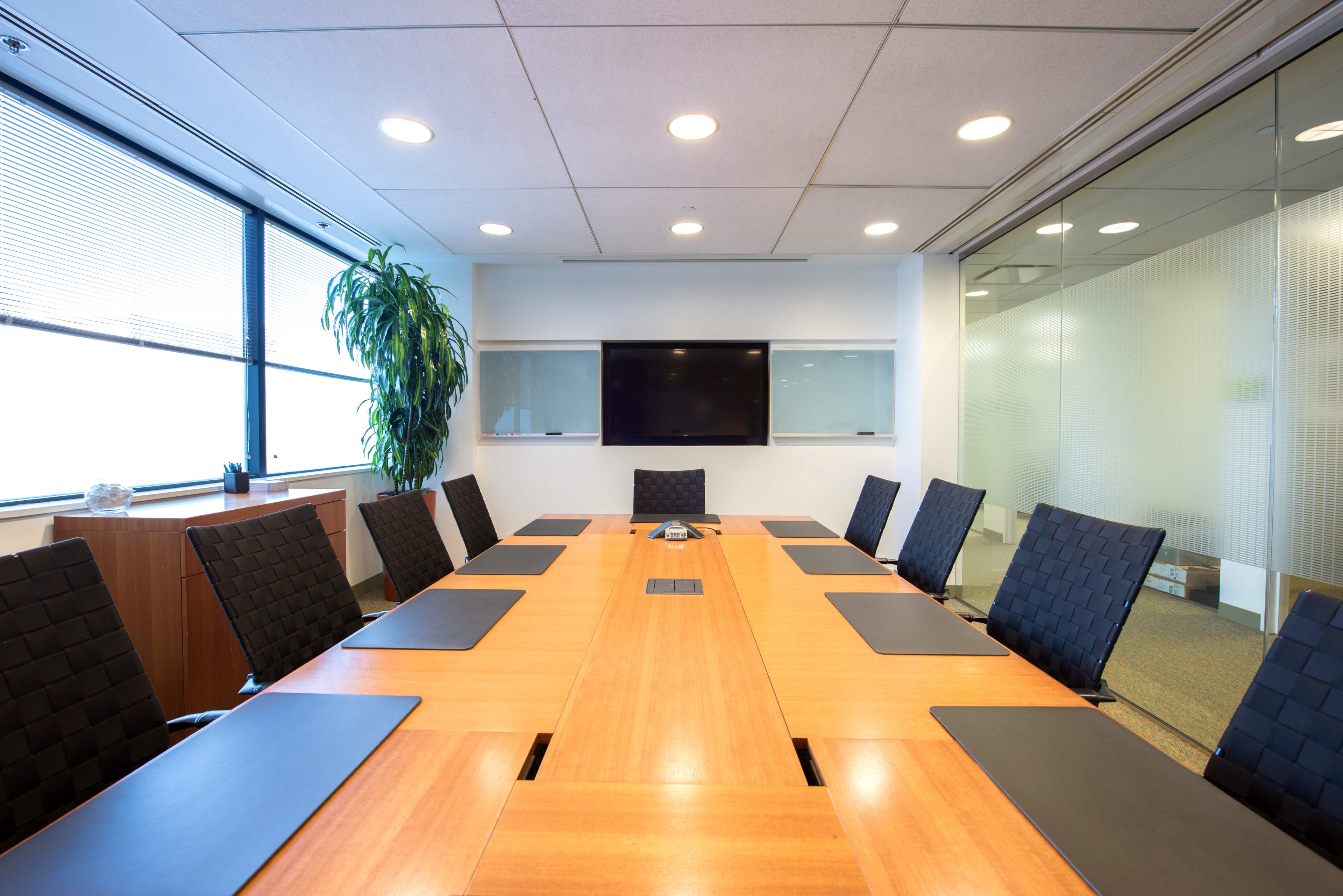 A conference room is set up with a long wooden table, black chairs, and a large screen on the wall.