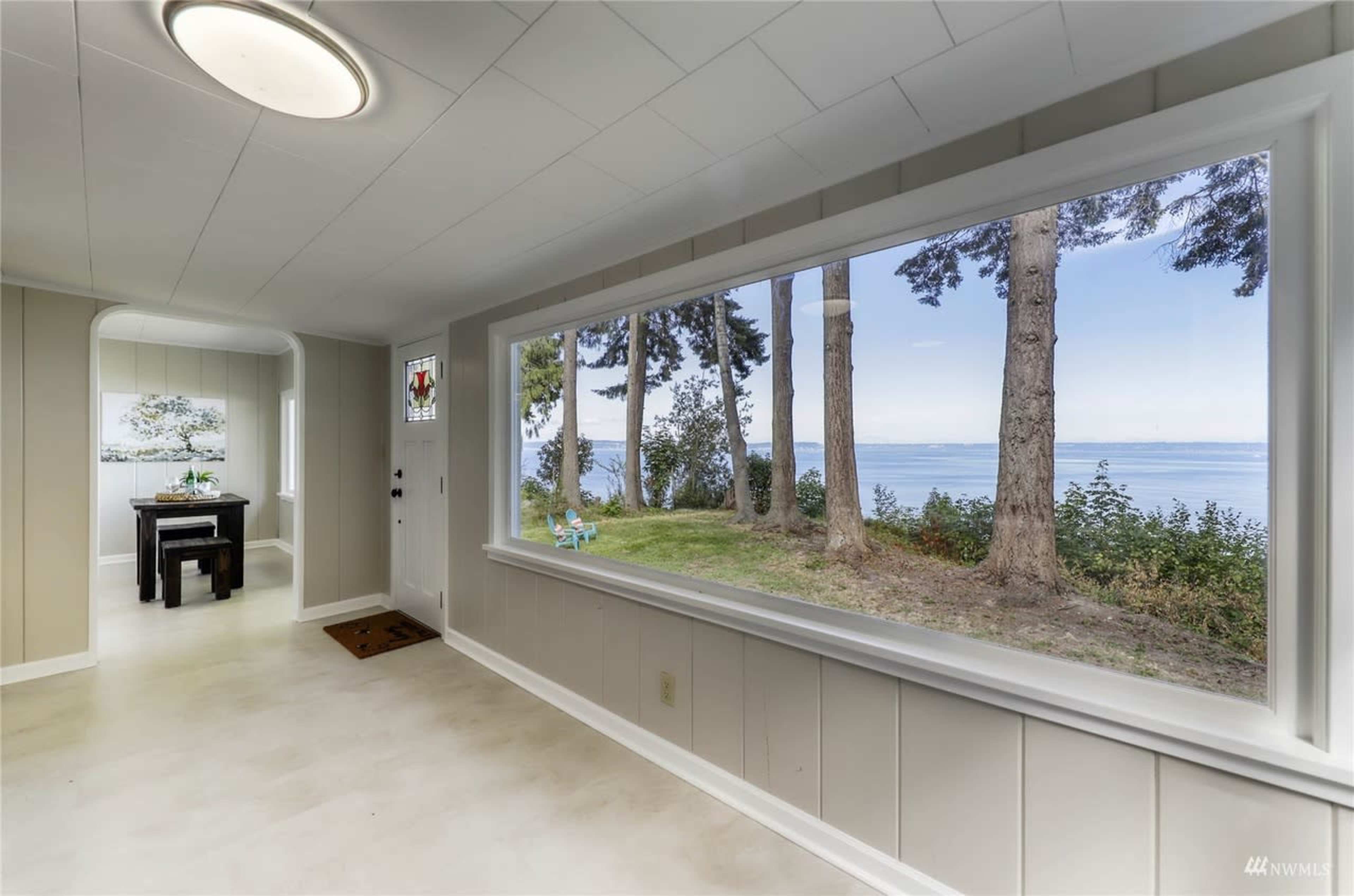 A bright interior room features a large window offering a view of trees and a body of water beyond.