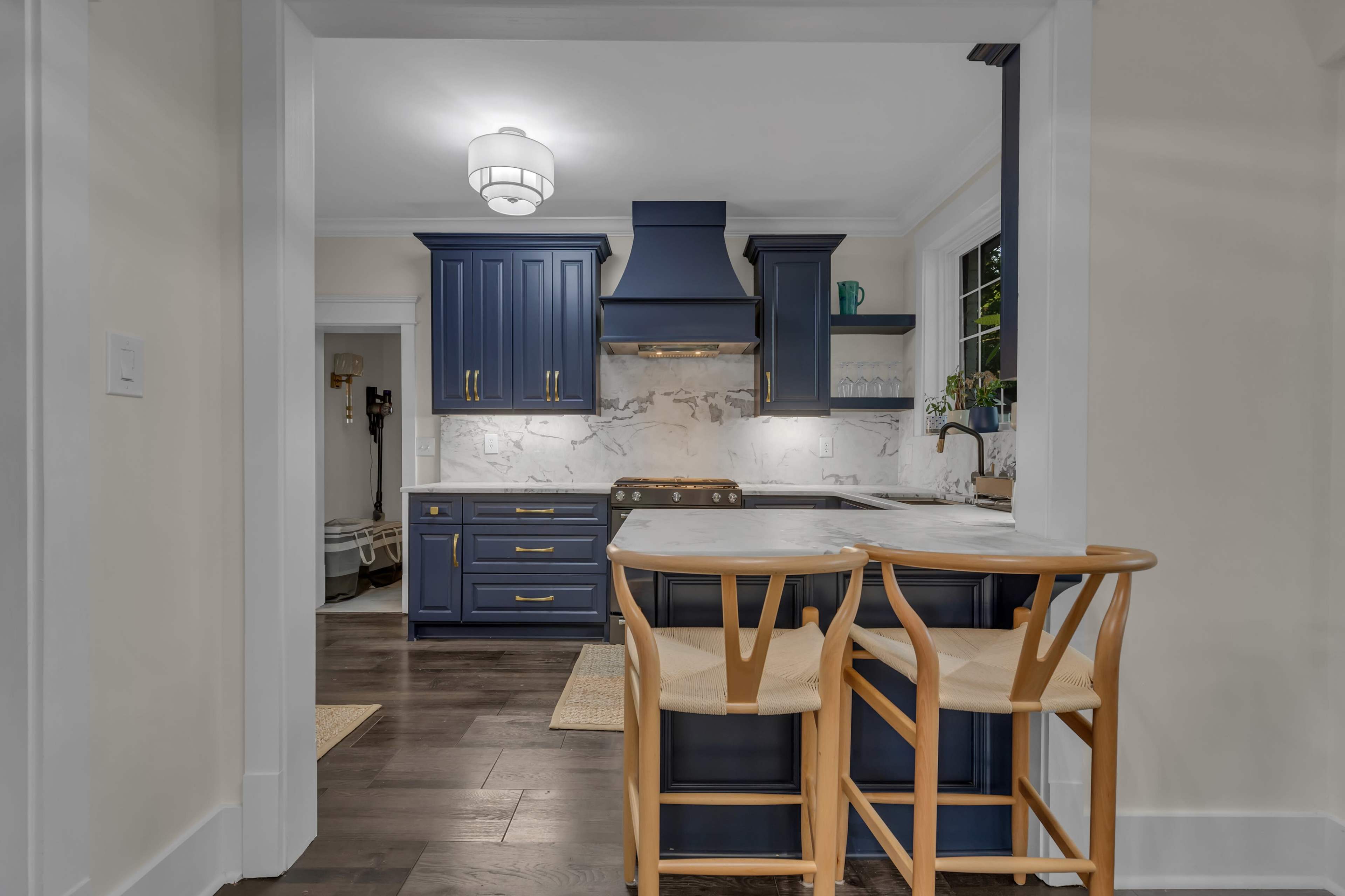 A modern kitchen features blue cabinetry, a marble countertop, and wooden bar stools near a breakfast bar.