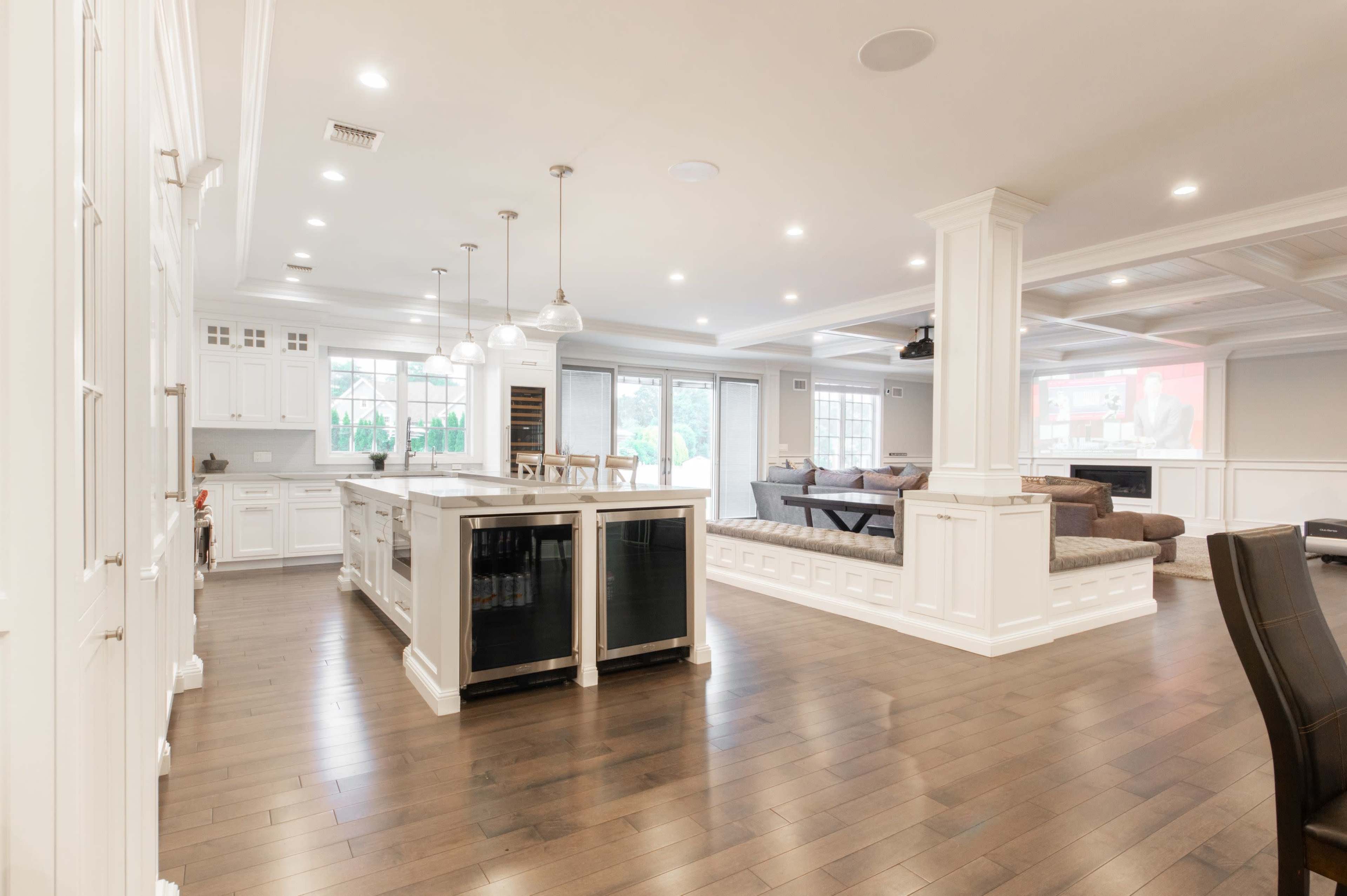 A modern kitchen and living room area with a large island, white cabinetry, and a beige sofa facing a television.