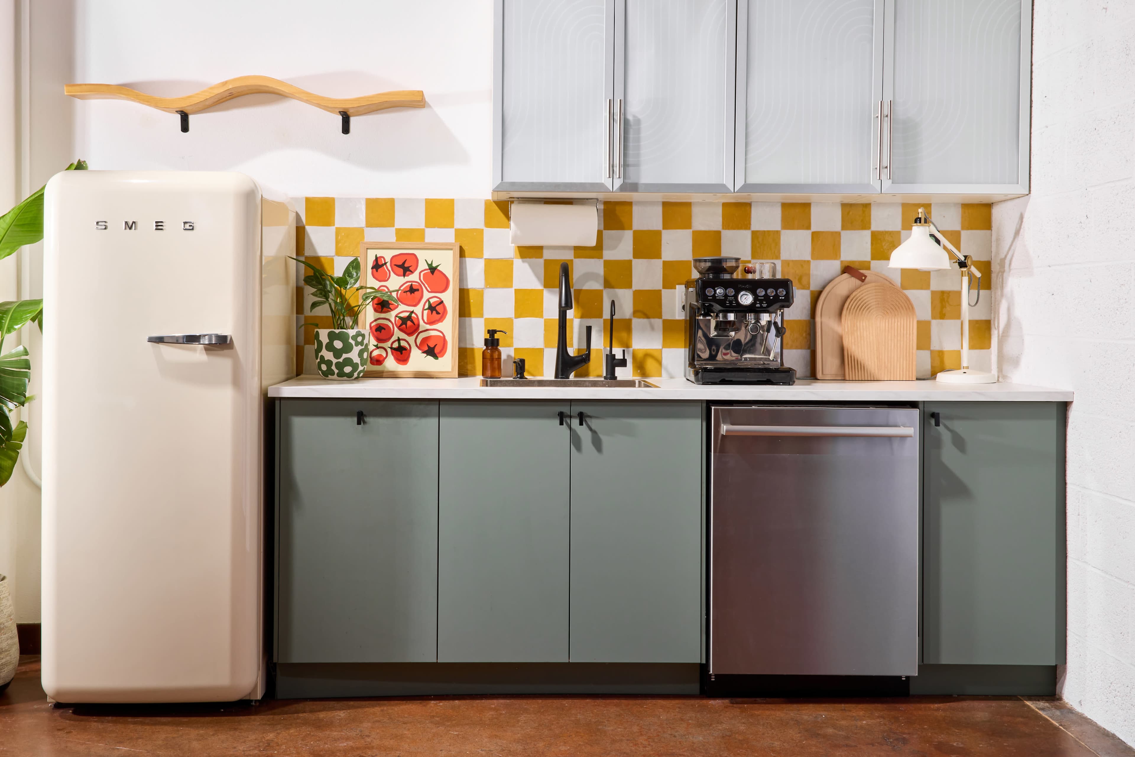 The image shows a modern kitchen featuring a cream-colored refrigerator, gray cabinets, a yellow and white tiled backsplash, and a coffee machine on the countertop.