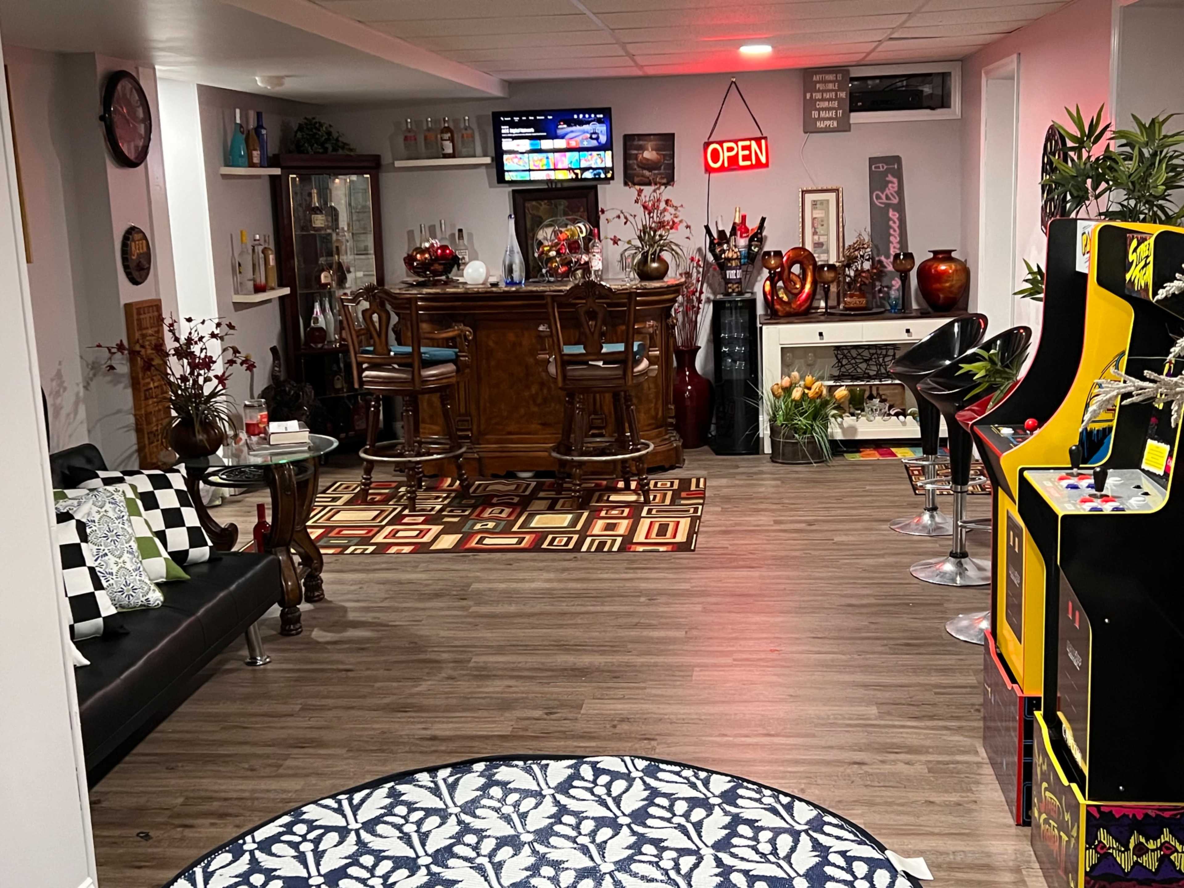 A well-decorated basement entertainment area features a bar with stools, a sofa, arcade machines, and various decorative elements.